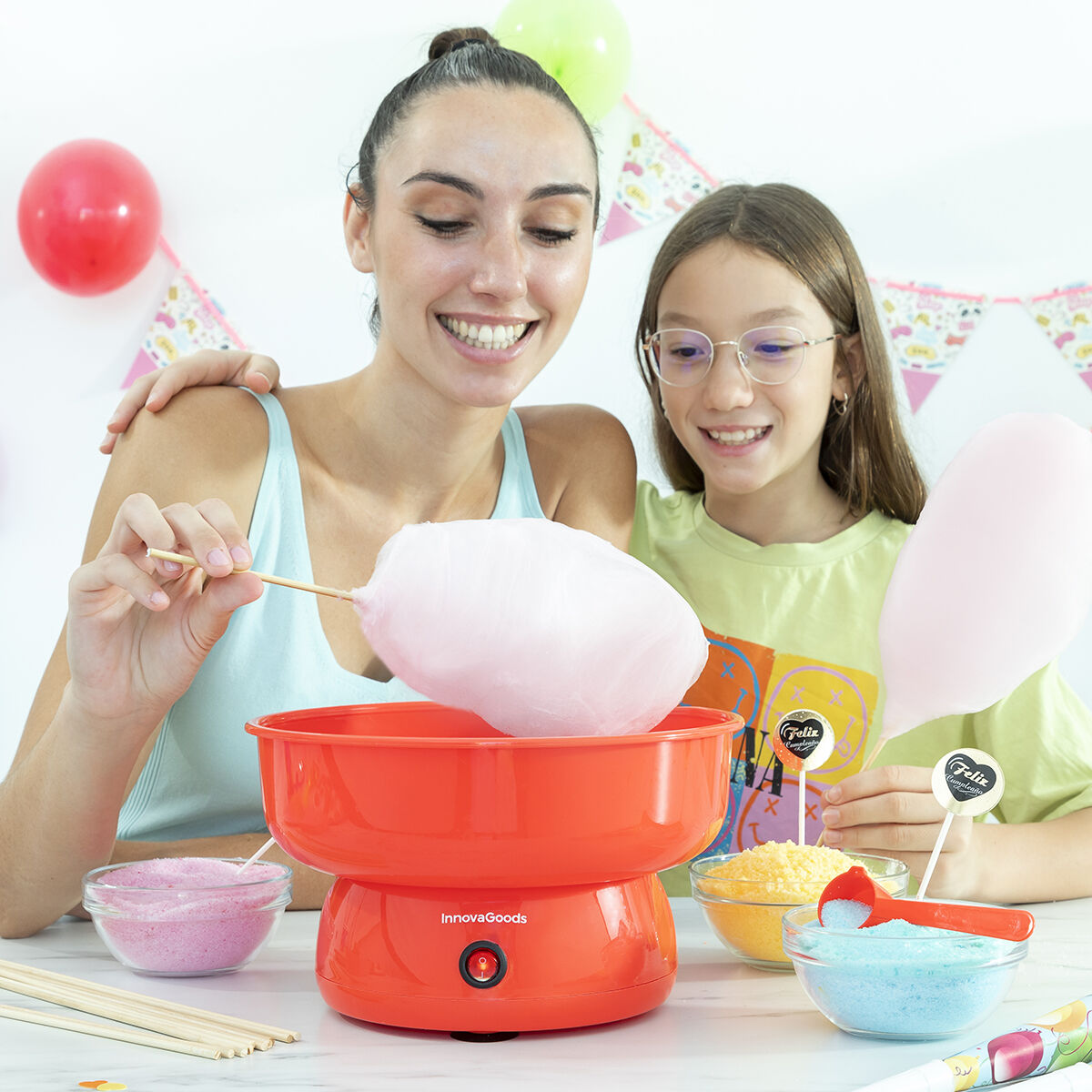 Zwei Frauen und ein Mädchen machen Zuckerwatte. Orangefarbene Maschine, rosa und blauer Zucker und Ballons.
