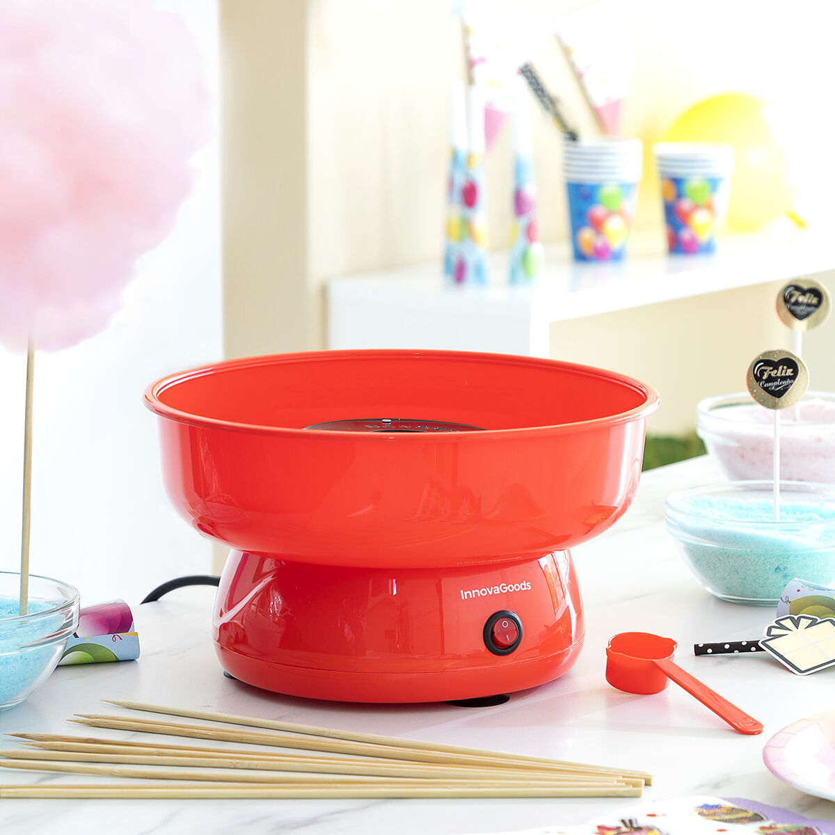 Eine rote Zuckerwattemaschine mit Zubehör. Sie steht auf einem weißen Tisch.
