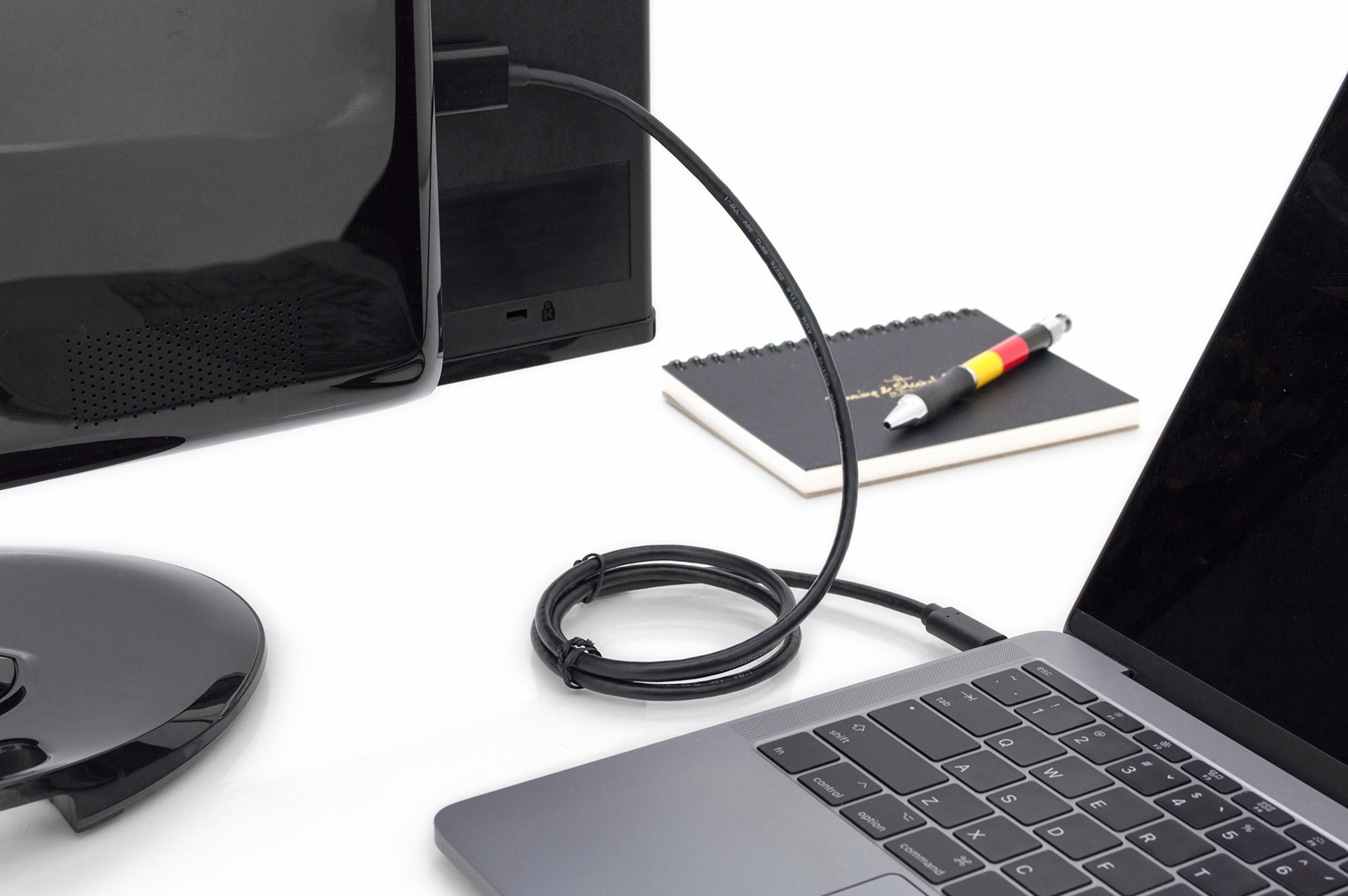 Laptop, der über ein schwarzes Kabel an einen Monitor angeschlossen ist, auf weißer Oberfläche.
