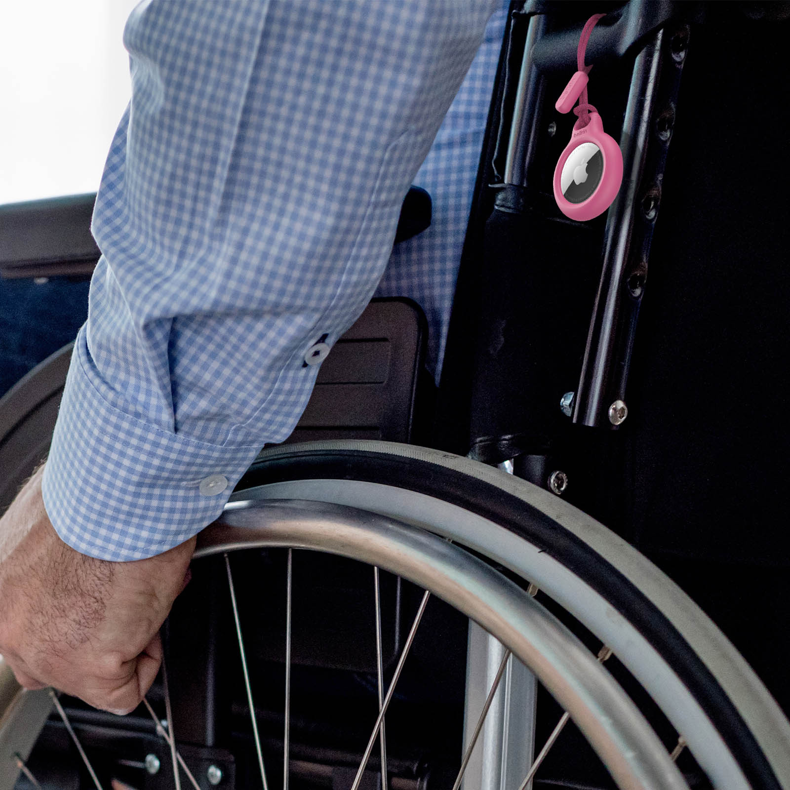 Osoba na wózku inwalidzkim, trzymająca koło, z różowym AirTagiem przymocowanym do krzesła.