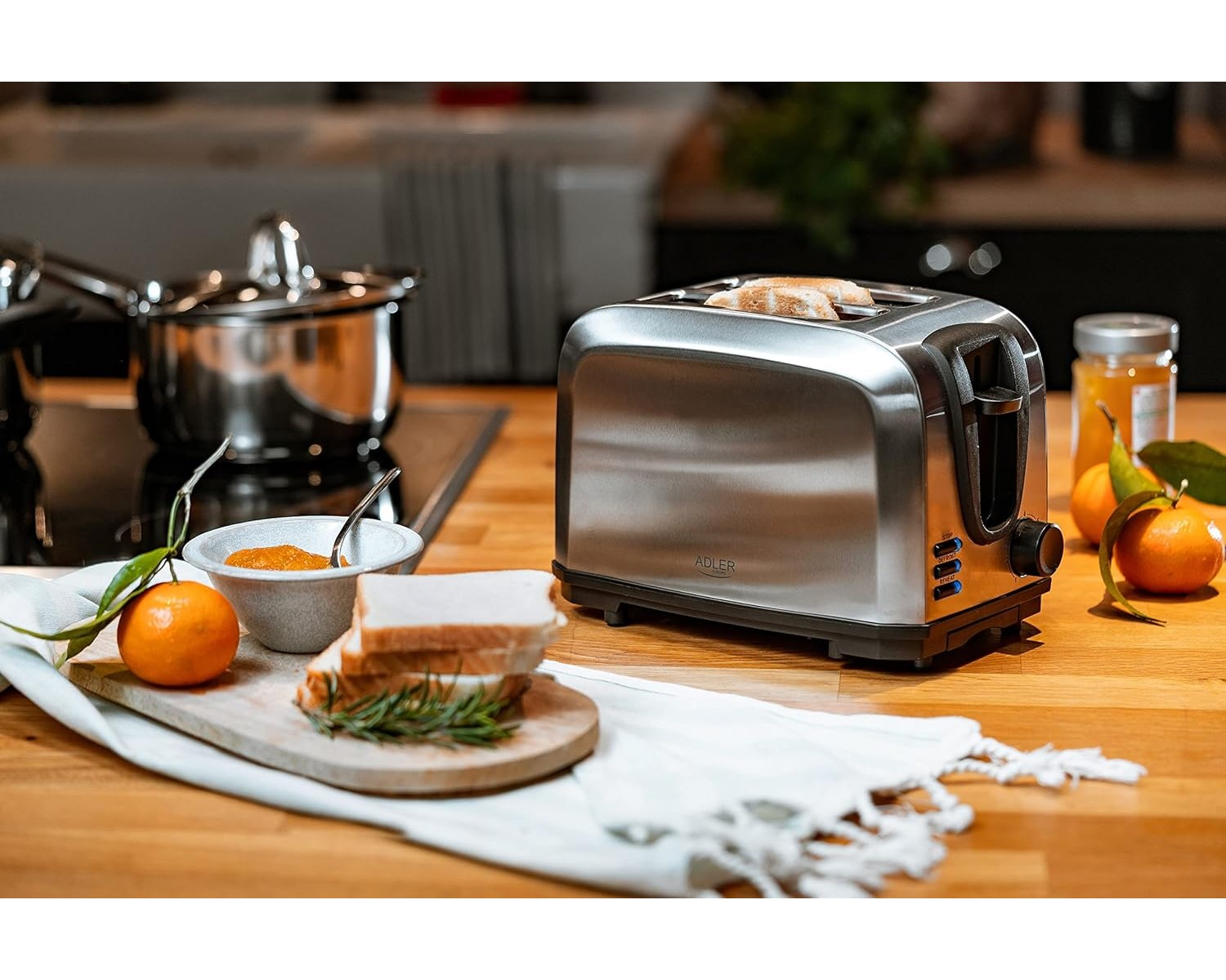 Silberner Toaster mit Brotscheiben. Orange und Marmelade stehen auf dem Holztisch. Küchenhintergrund.