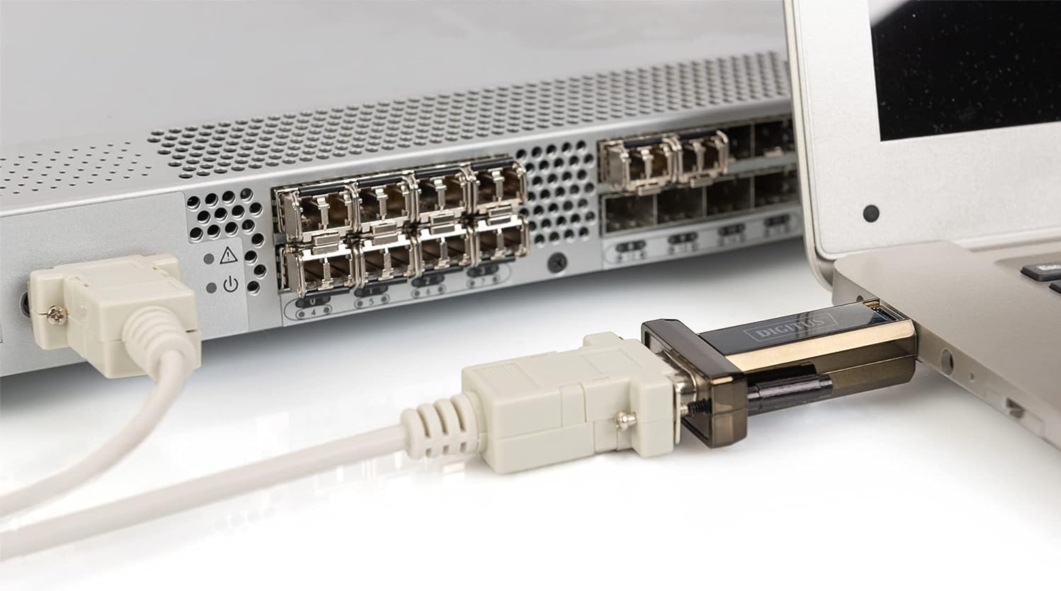 Przełącznik sieciowy z różnymi portami, podłączony do laptopa za pomocą białego kabla i adaptera USB.