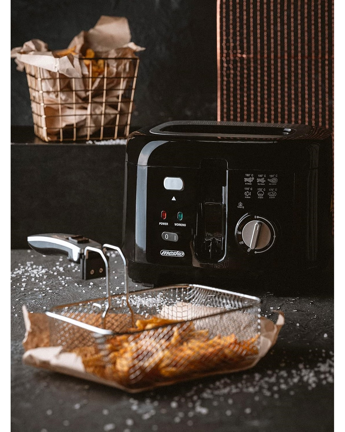 Eine schwarze Fritteuse mit silbernem Griff und einem Korb mit Pommes Frites. Es gibt auch einen Salzkorb.