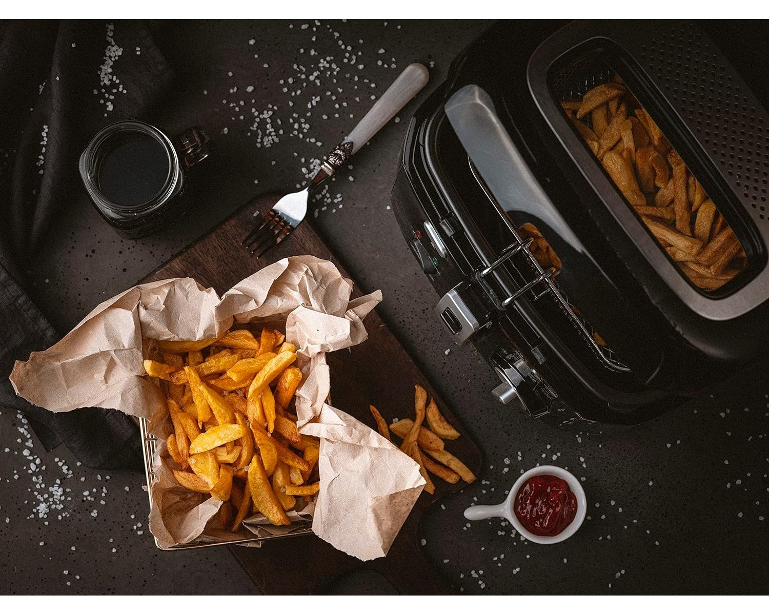 Draufsicht auf Pommes Frites in einem Korb und eine kleine Schüssel Ketchup auf einem Tisch.