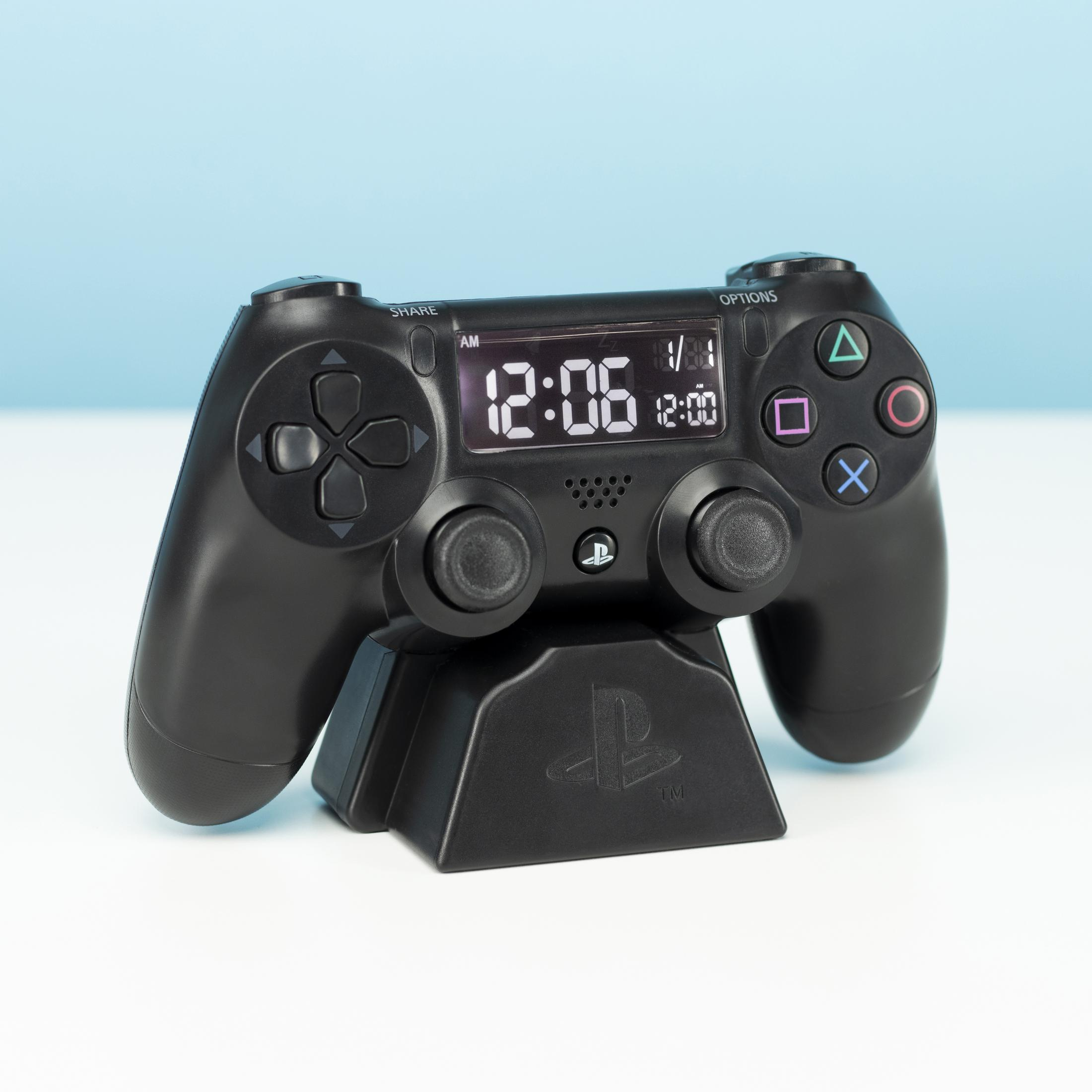 Schwarzer PS4-Controller, Ladestation mit PS-Logo. Digitaluhr zeigt die Uhrzeit an. Blau-weißer Hintergrund.