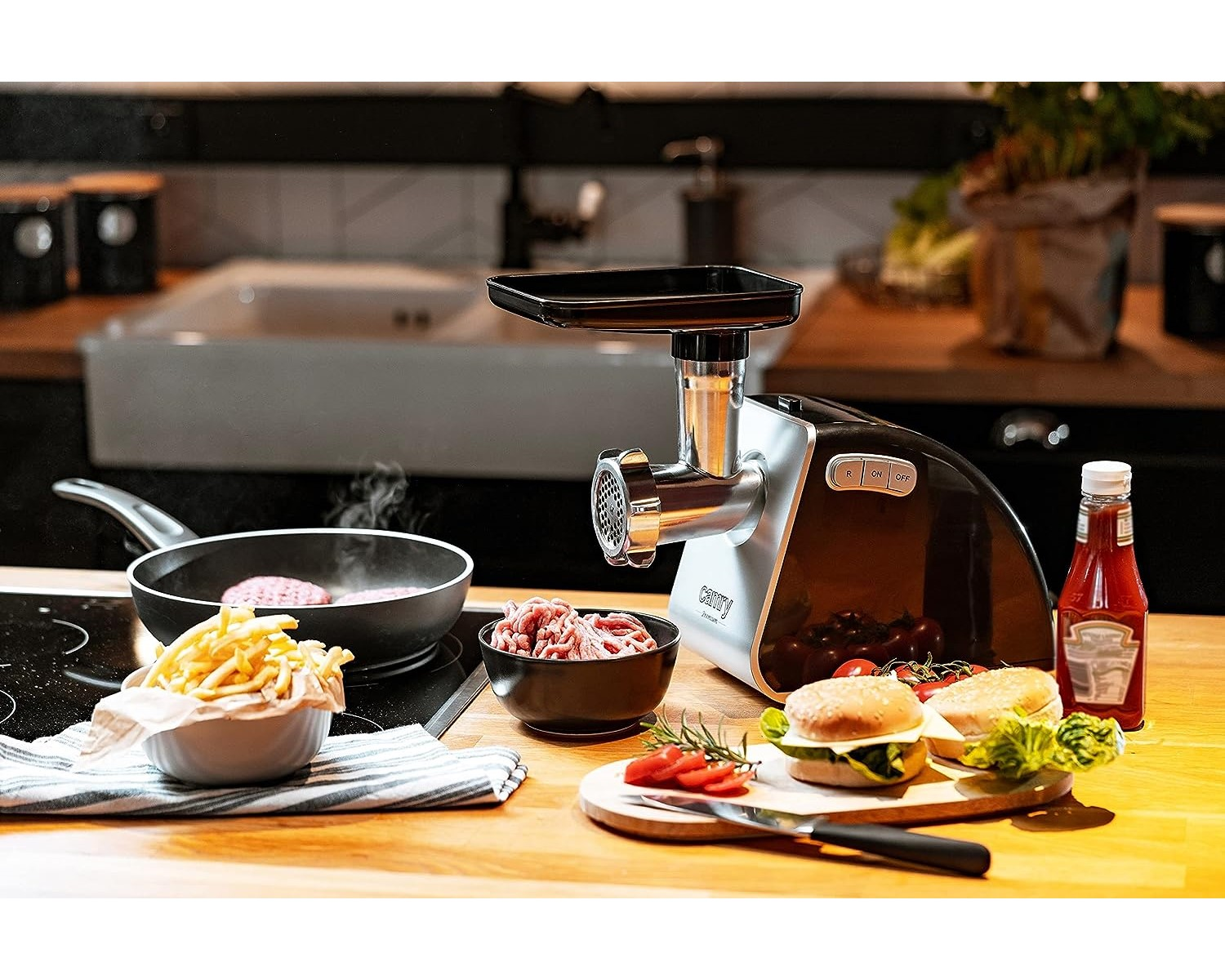 Eine Küchenszene mit Fleischwolf, Pommes Frites, Burgerzutaten und einer Bratpfanne mit einem Patty.