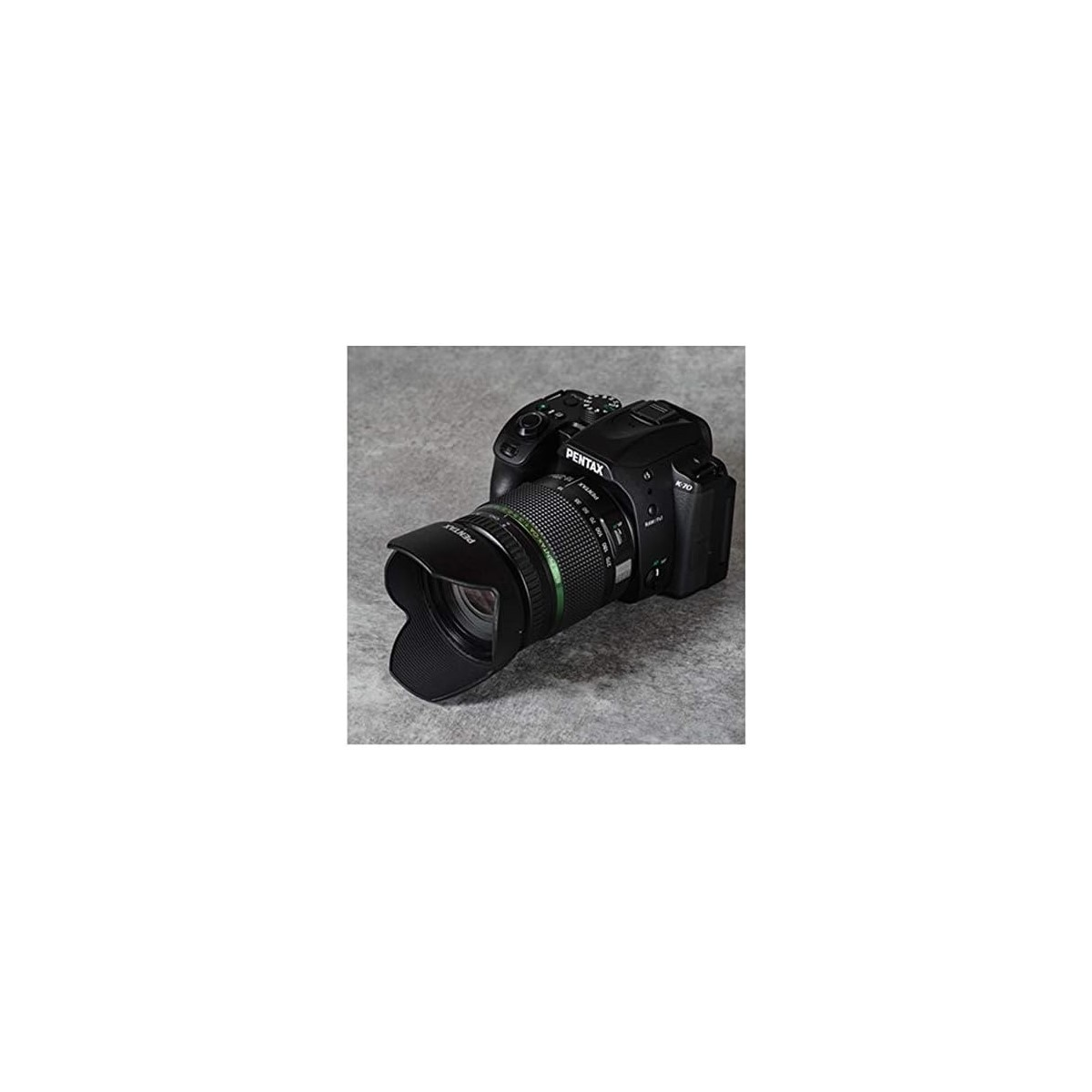Schwarze Pentax-Kamera mit nach links gerichtetem Objektiv auf grauem Untergrund.