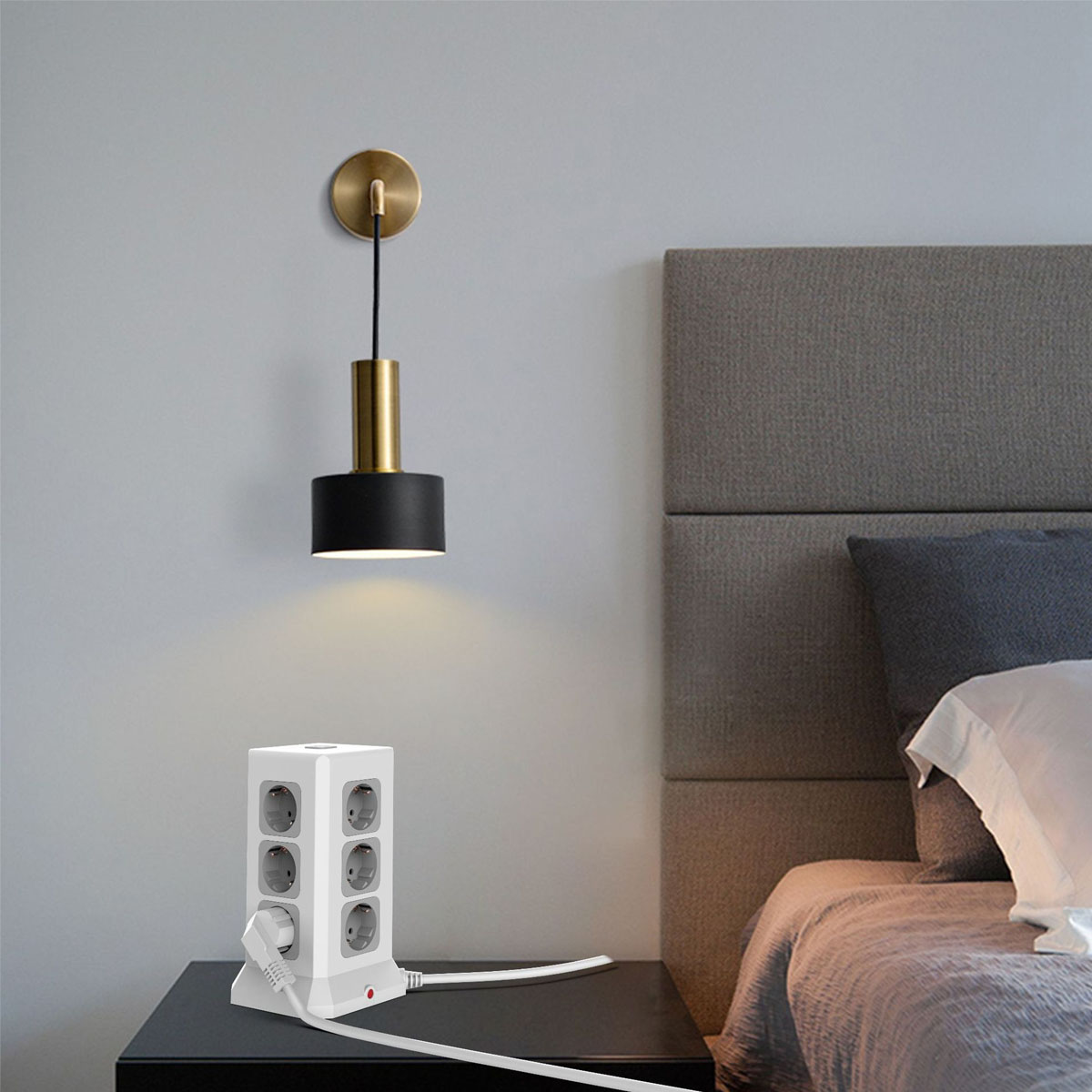 Eine weiße Steckdosenleiste neben einer Wandleuchte. Im Hintergrund befindet sich ein Bett.