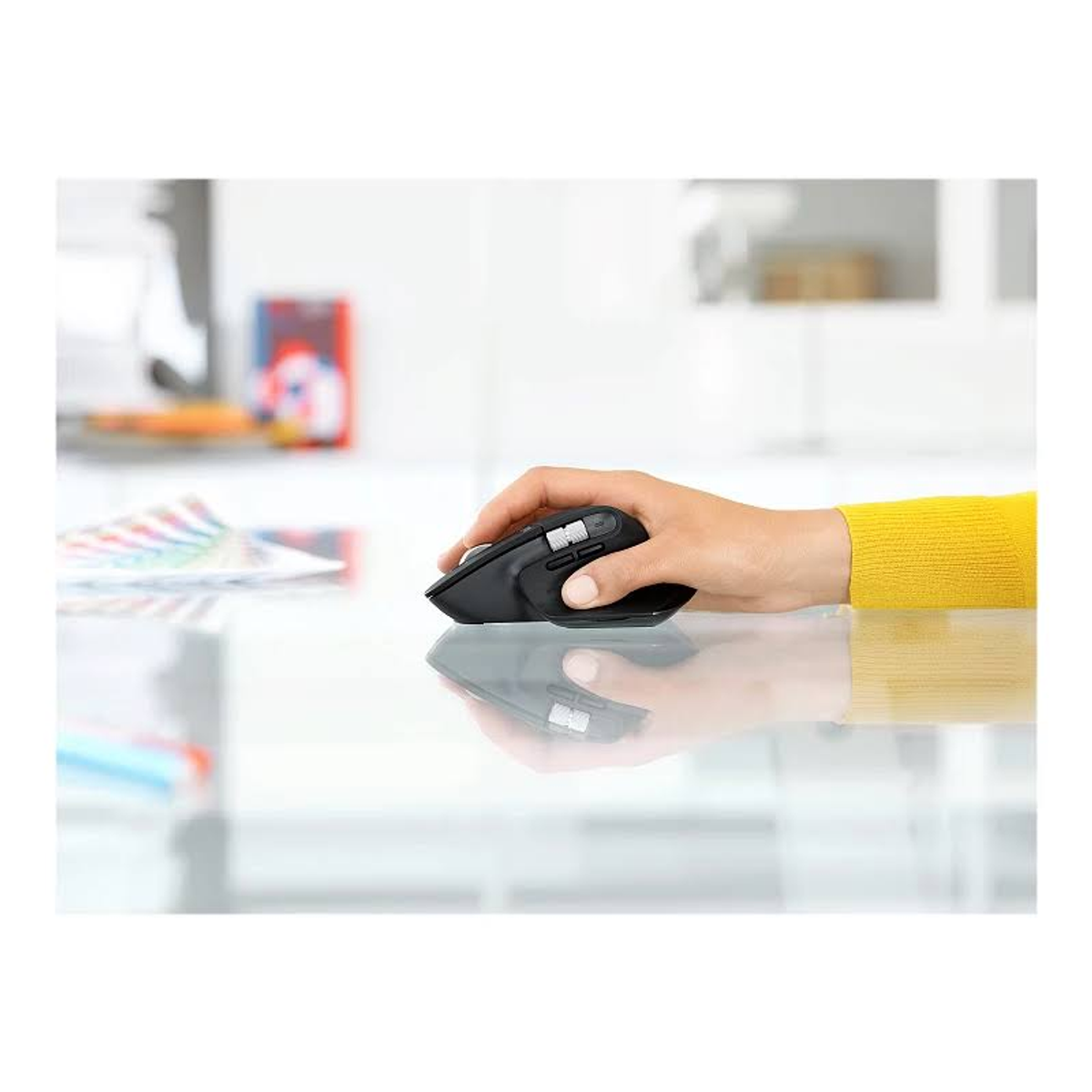 Main utilisant une souris noire sur une surface vitrée. Manchon jaune visible.