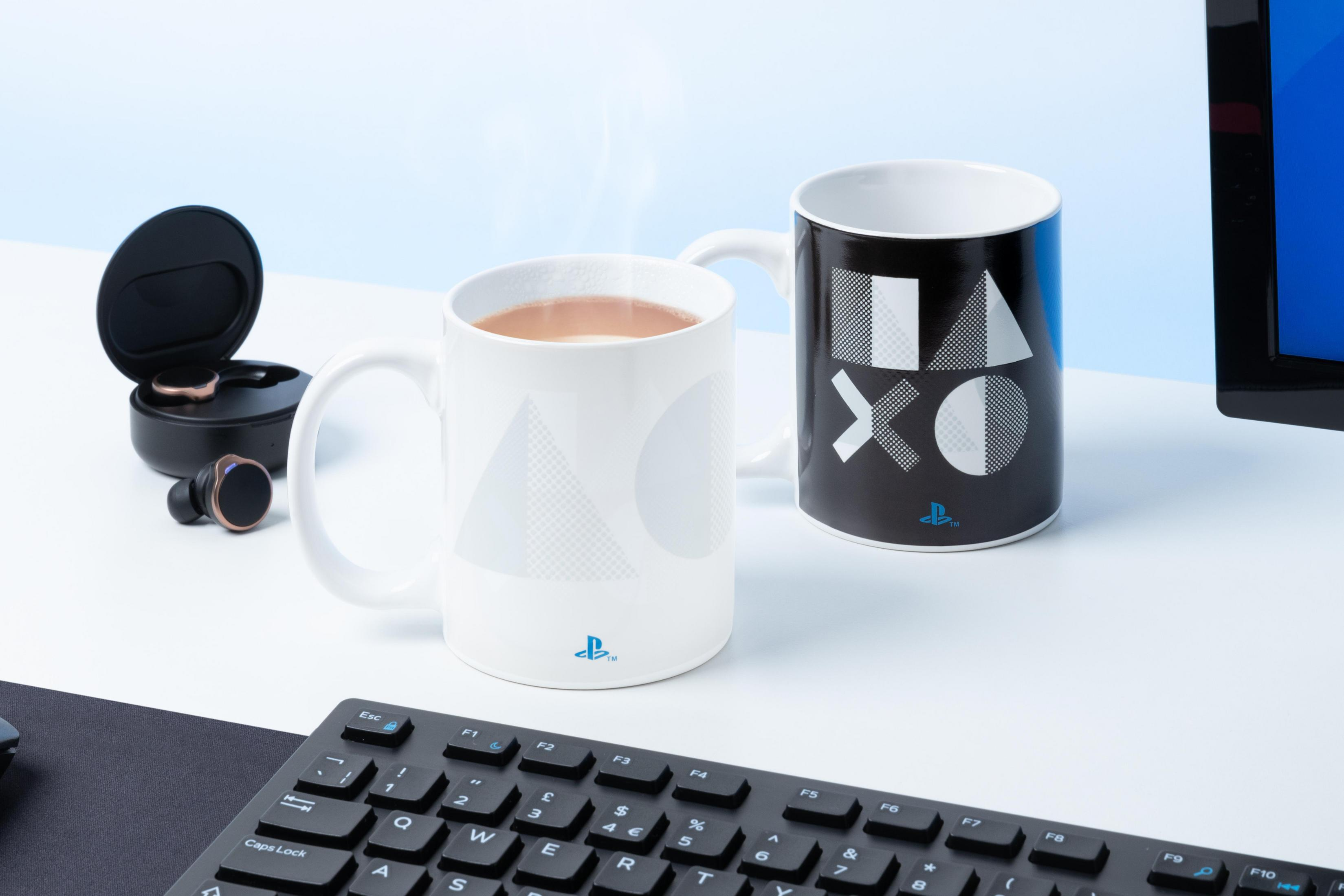 Zwei PlayStation-Tassen mit Logos. Eine weiße mit Symbolen, eine schwarze mit Symbolen. Tastatur im Hintergrund.