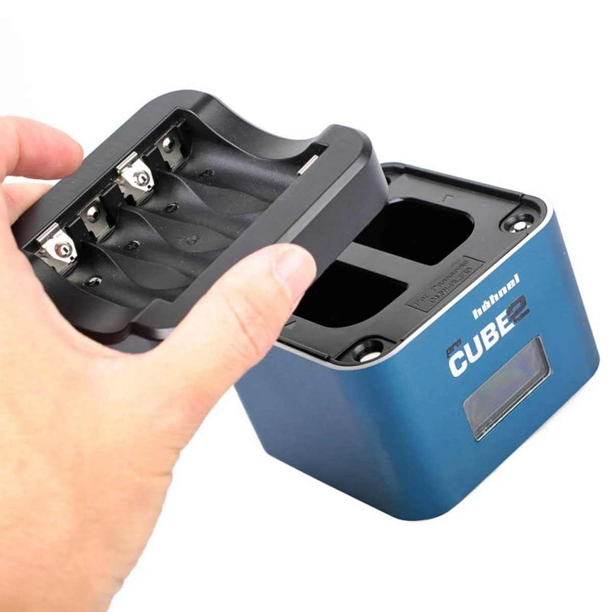 Hand öffnet ein schwarzes Batterieladegerät mit vier Schlitzen und blauem Sockel, weißer Hintergrund.