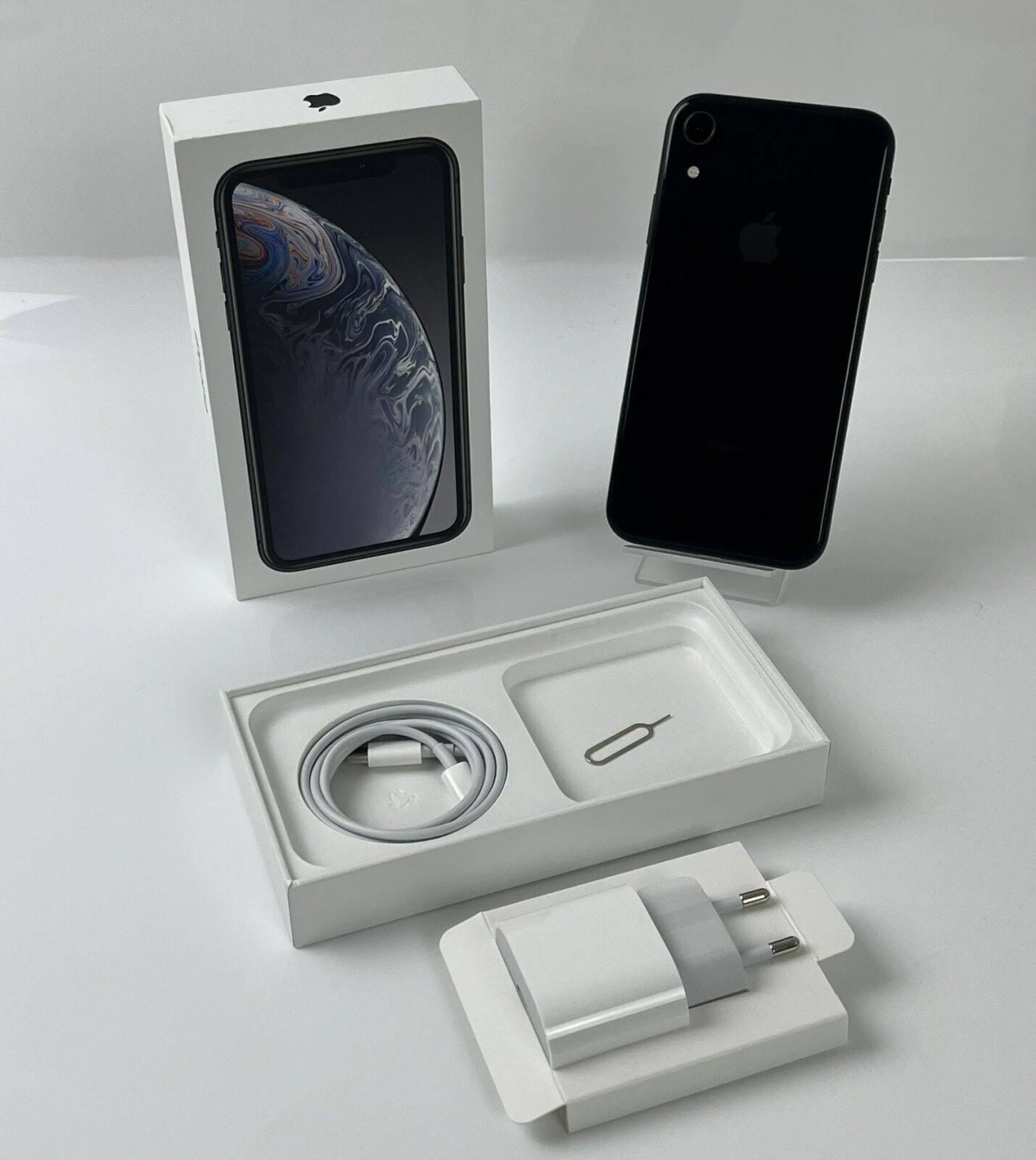 Ausgepacktes iPhone XR mit Zubehör, einschließlich Ladekabel und Netzteil, auf Weiß.