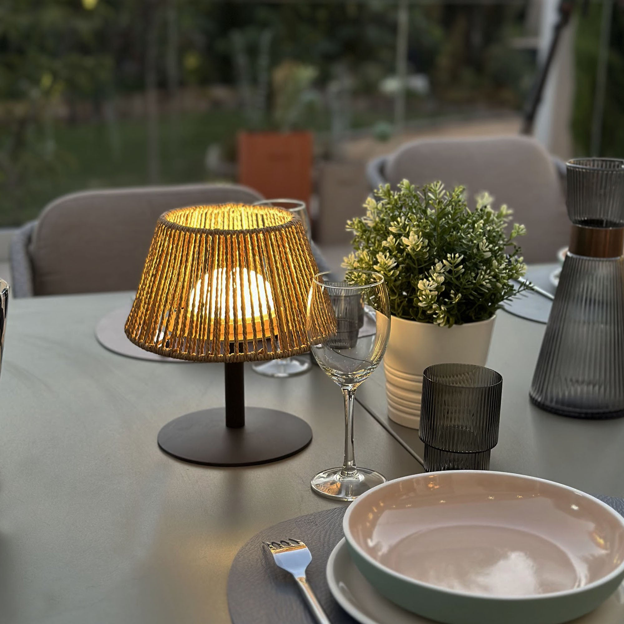 Tischdekoration mit einer beleuchteten Lampe. Lampe mit Korbschirm, Gläsern und einer Schüssel.