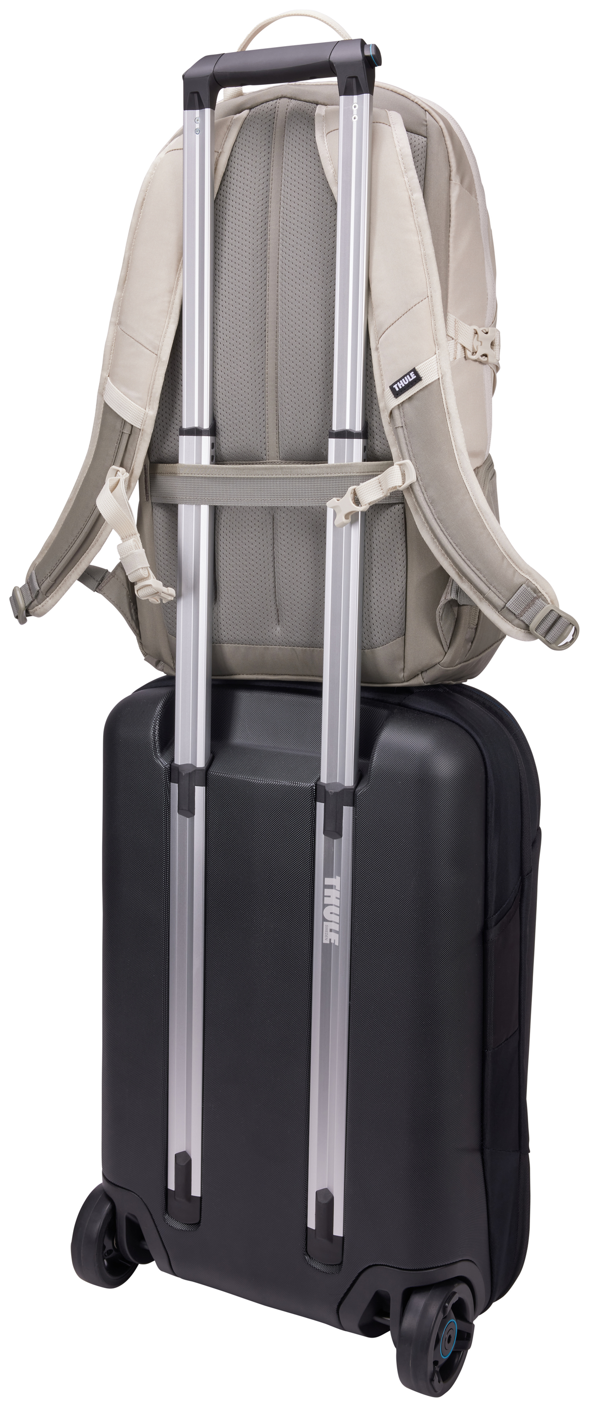 Ein beiger Rucksack auf einem schwarzen Rollkoffer mit silbernen Griffen.