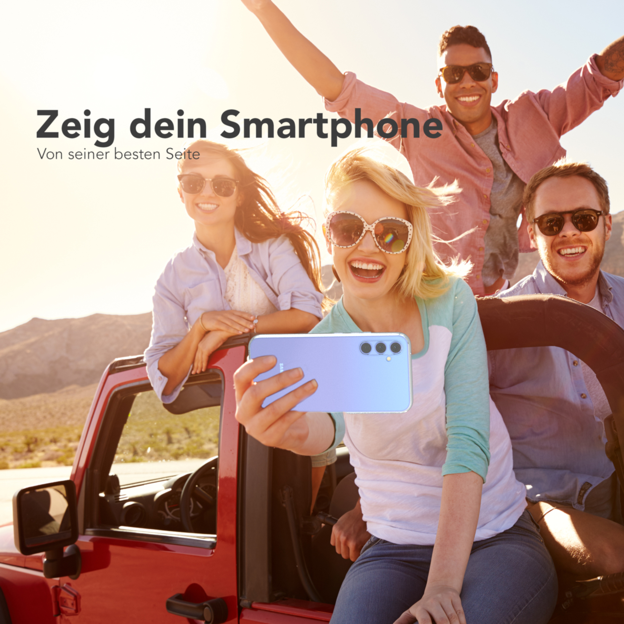 Gruppe von Leuten, die ein Selfie in einem roten Auto machen und ein hellblaues Telefon halten.