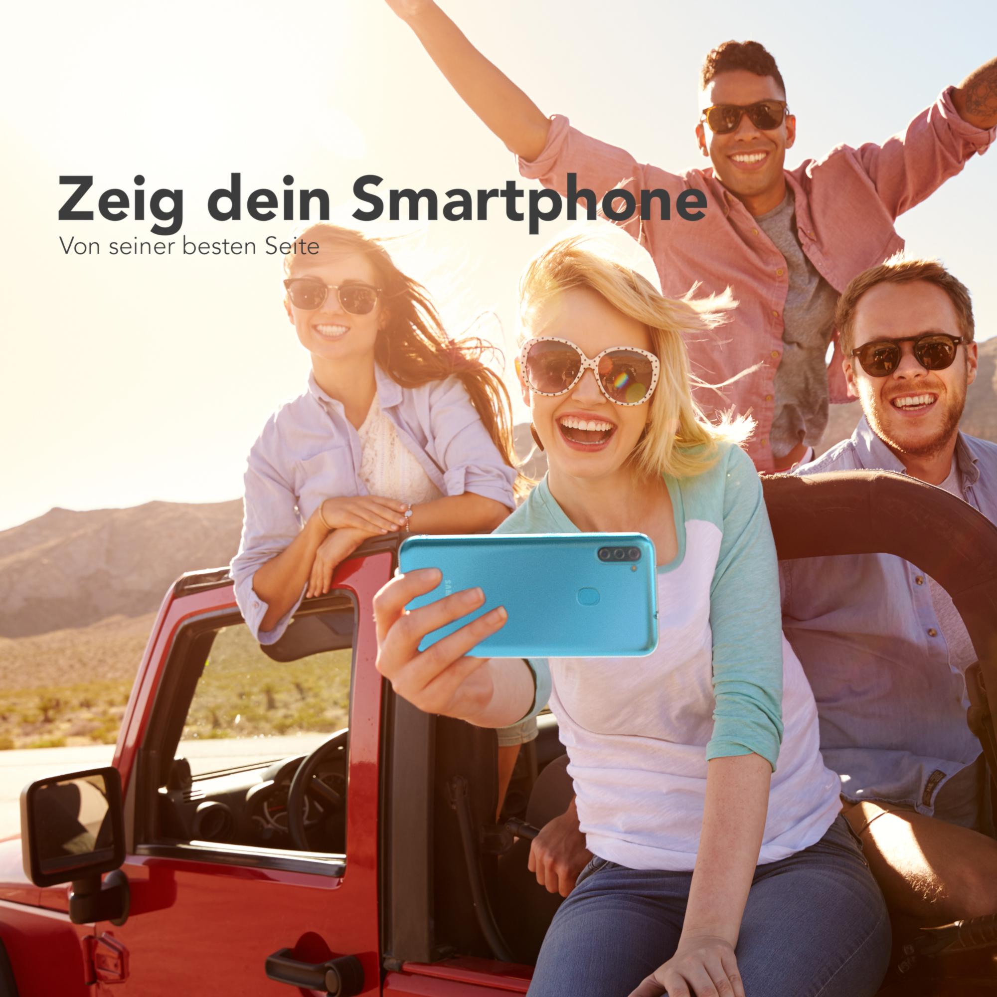 Vier Personen in einem Auto machen ein Selfie mit einem Telefon. Text: 'Zeig dein Smartphone'.