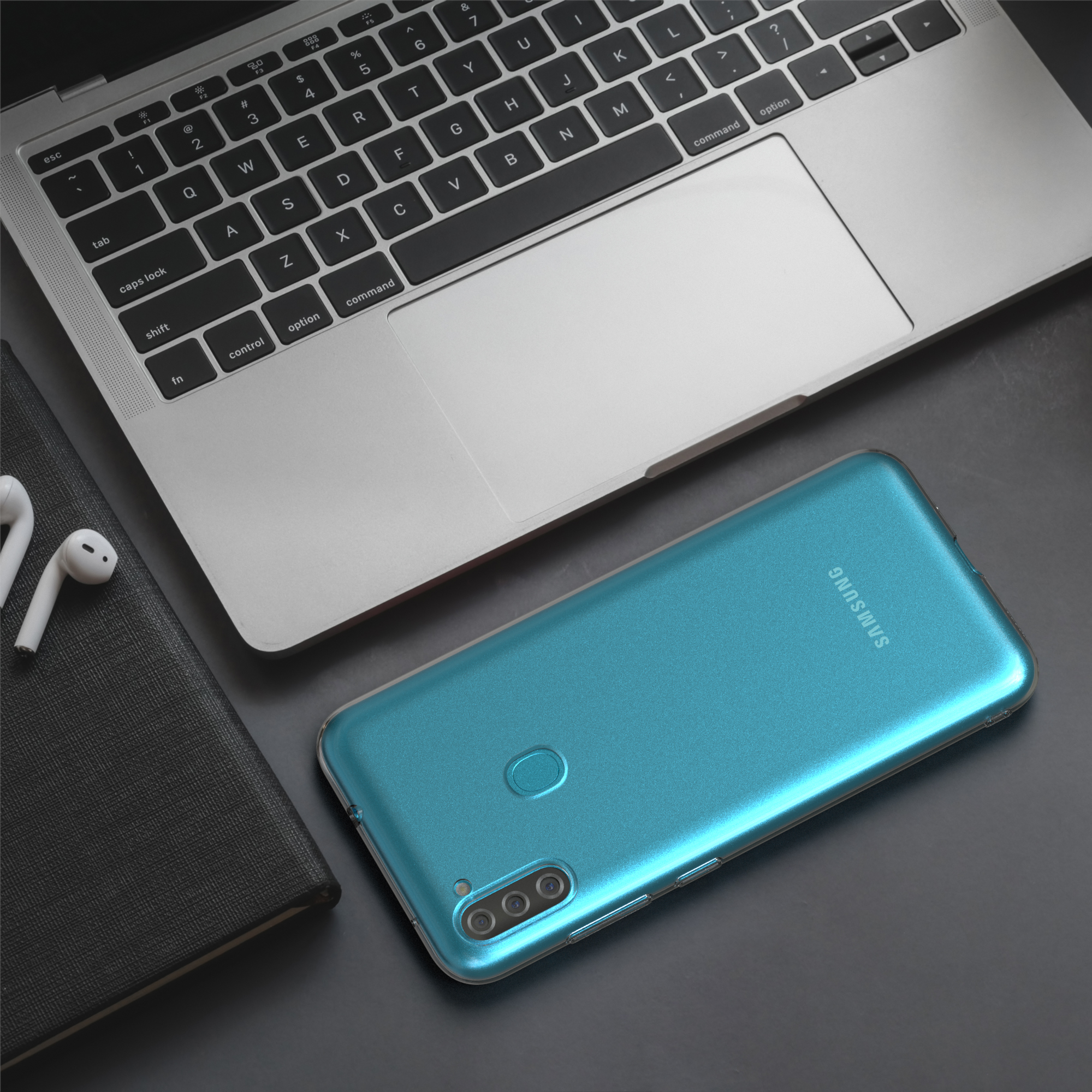 Laptop, Telefon und Kopfhörer auf dunkler Oberfläche. Das Telefon ist blau und der Laptop silberfarben.