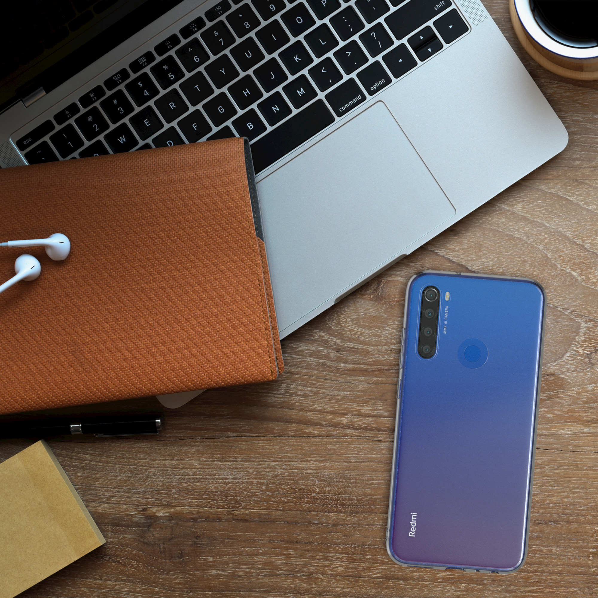 Blaues Telefon in klarer Hülle auf einem Holztisch, mit Laptop, Notizbuch und Ohrhörern. Draufsicht.