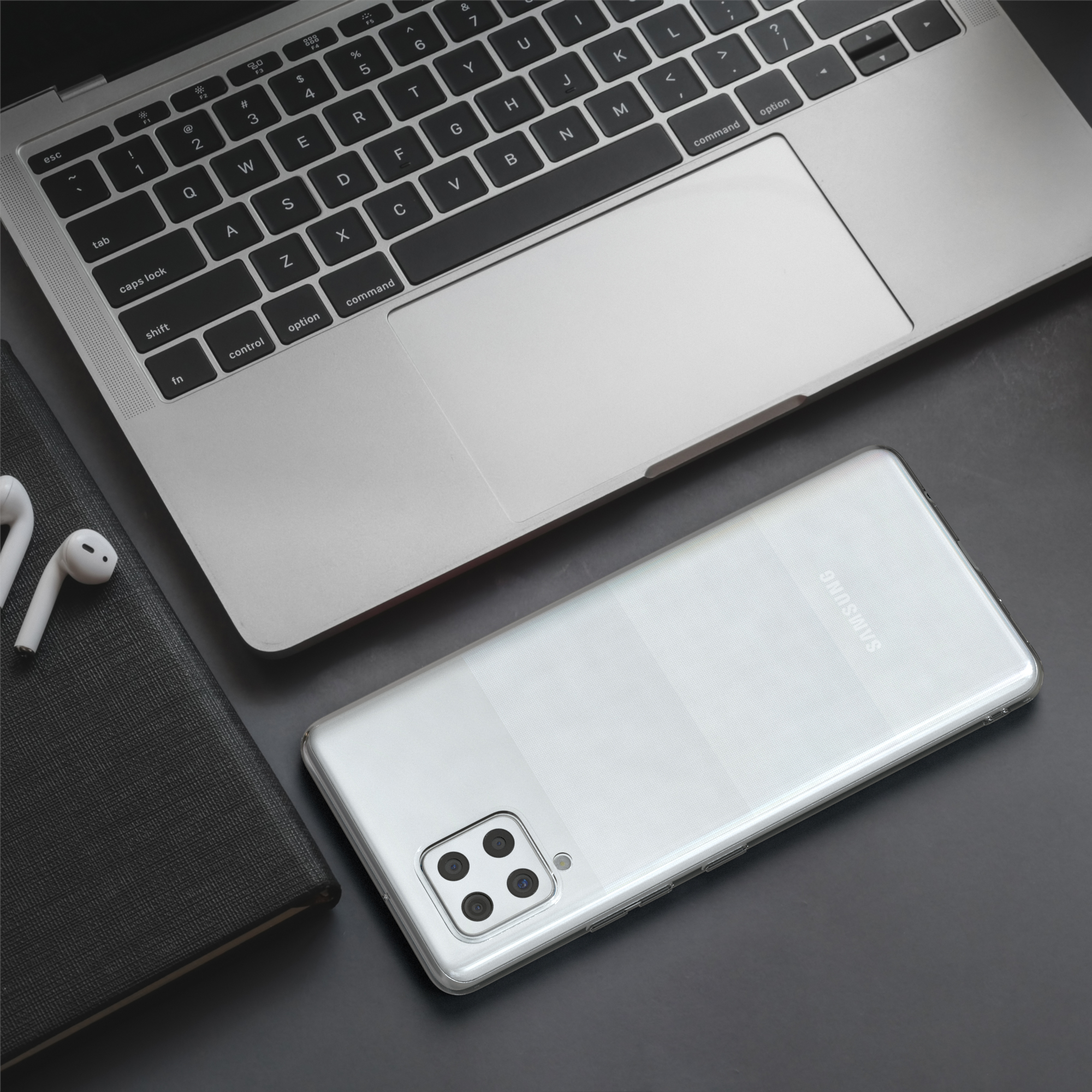 Laptop mit weißem Telefon und Ohrhörern links. Ein silbernes Samsung-Telefon liegt in der Mitte.