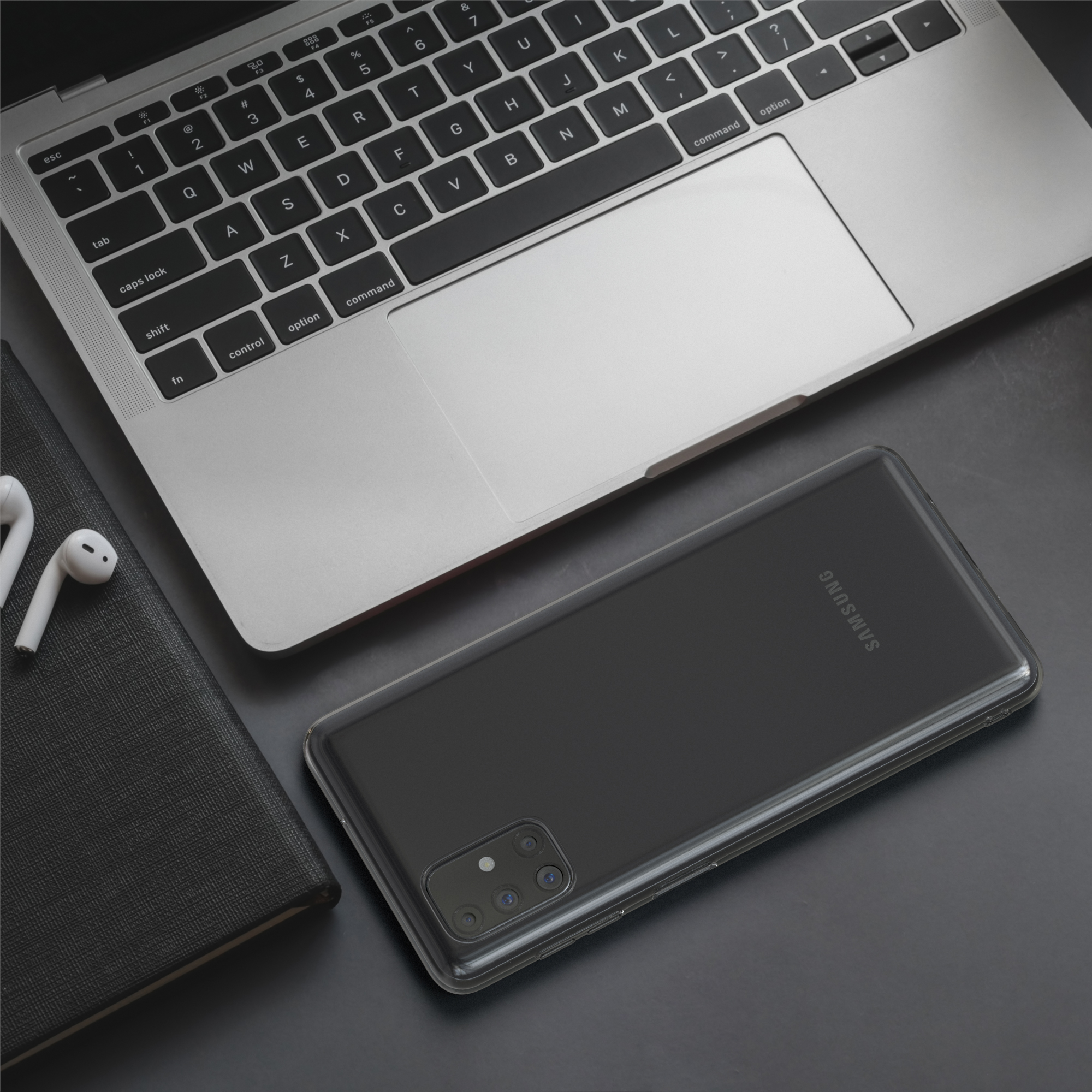 Smartphone auf dem Schreibtisch, mit Laptop und Zubehör. Schwarze Handyhülle sichtbar. Dunkler Hintergrund.