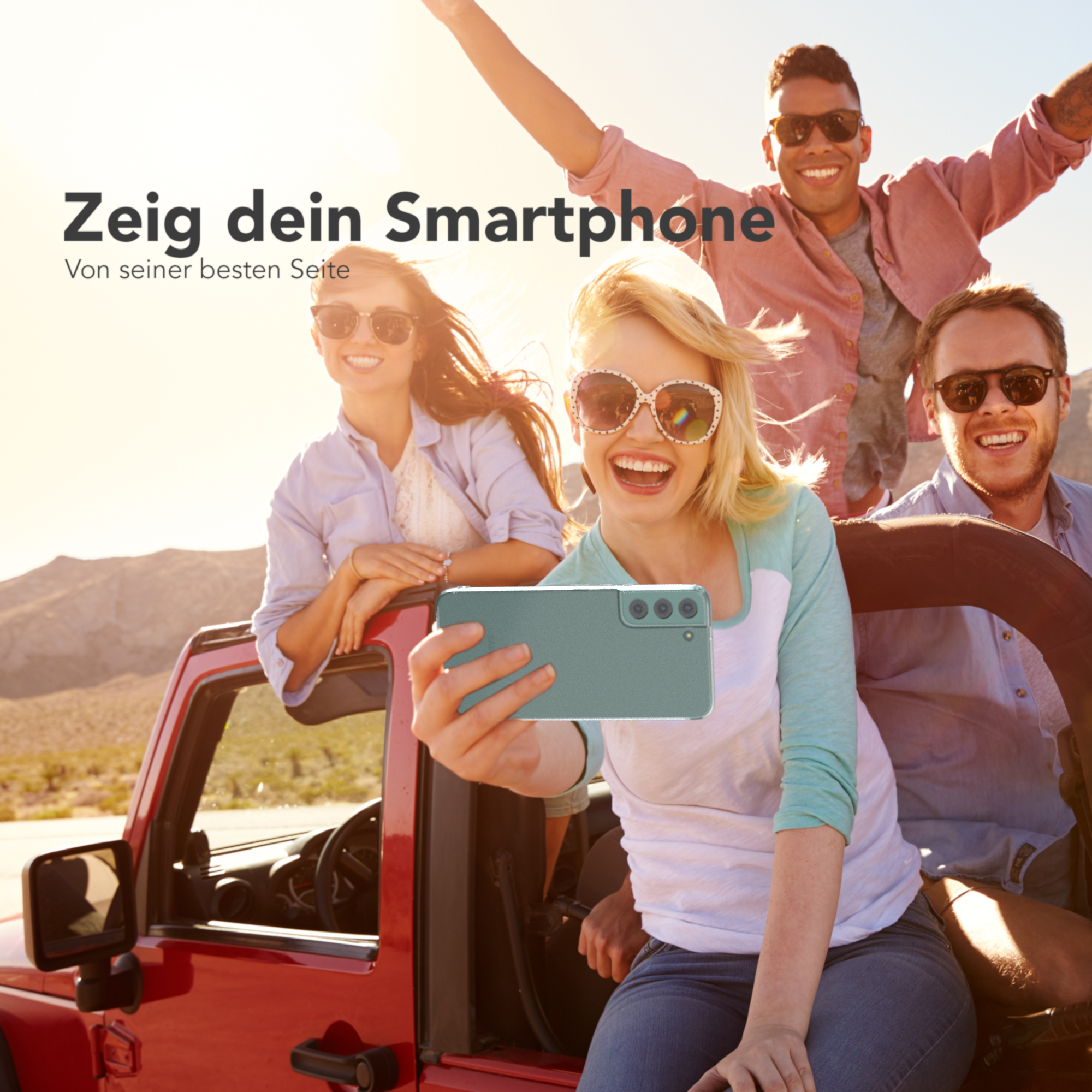 Vier Personen in einem roten Jeep machen ein Selfie mit einem Telefon. Die Sonne scheint im Hintergrund.