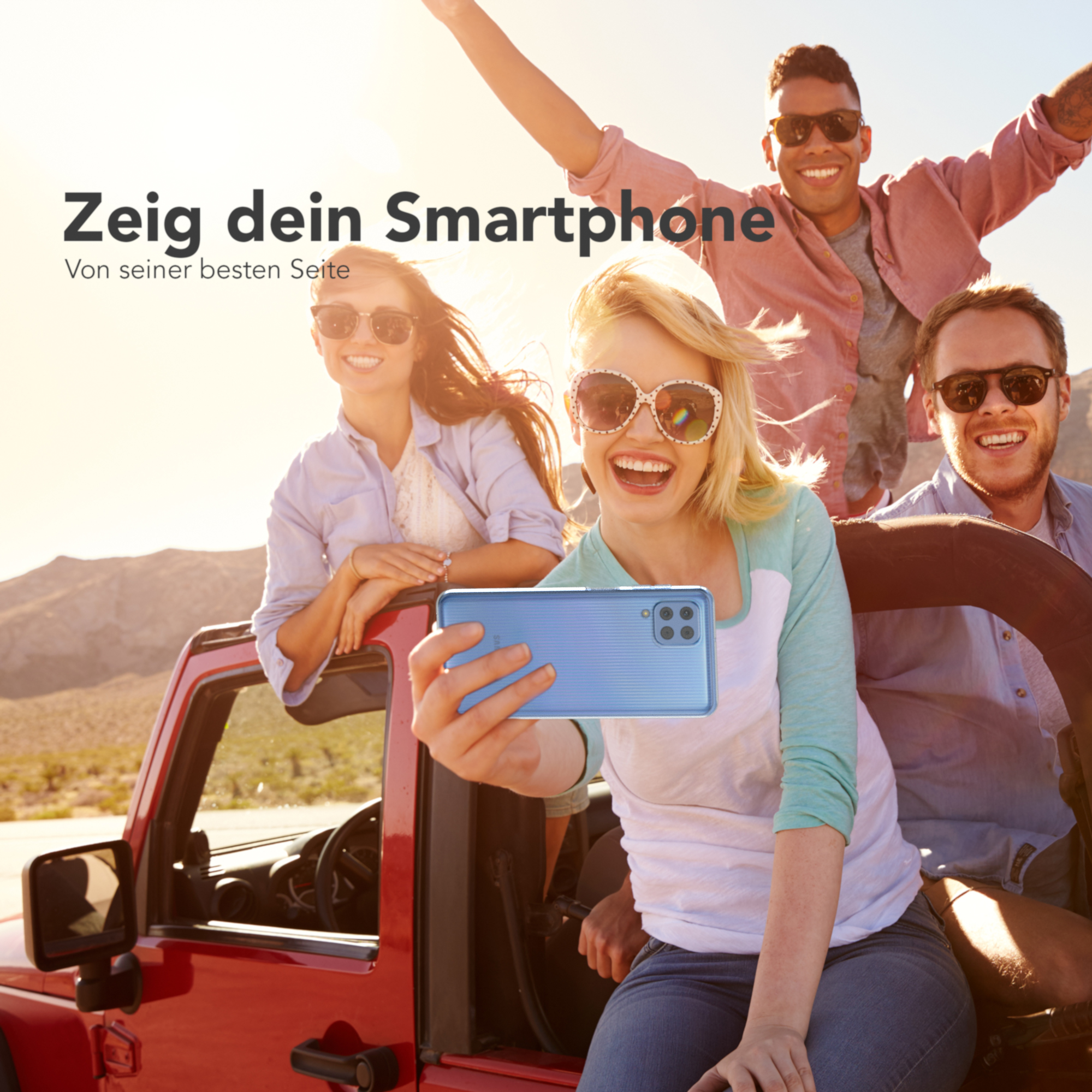 Vier Personen in einem roten Jeep machen ein Selfie mit einem Telefon. Sie lächeln und sind glücklich.