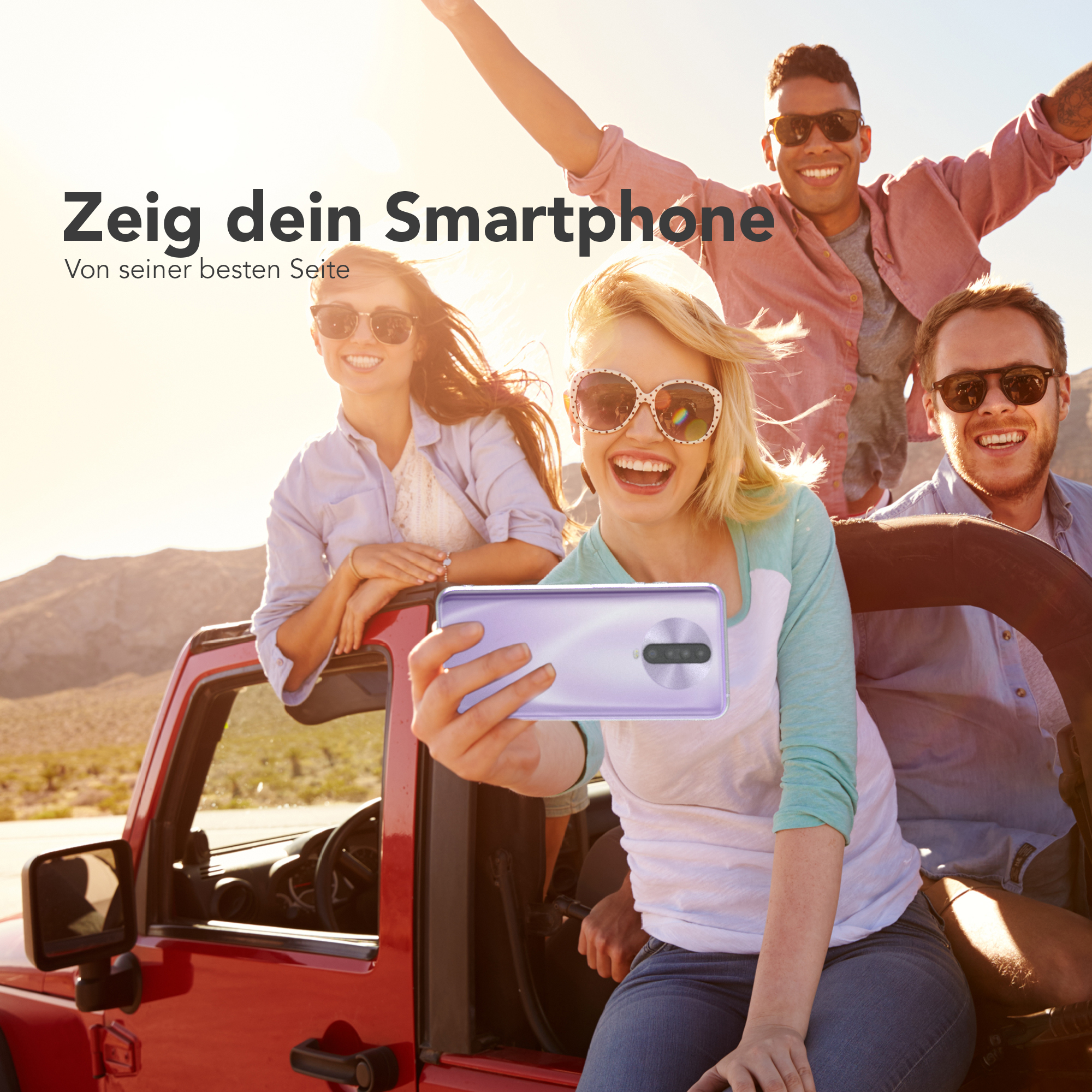 Eine Gruppe von vier Personen macht ein Selfie mit einem Telefon. Sie sind in einem roten Auto.
