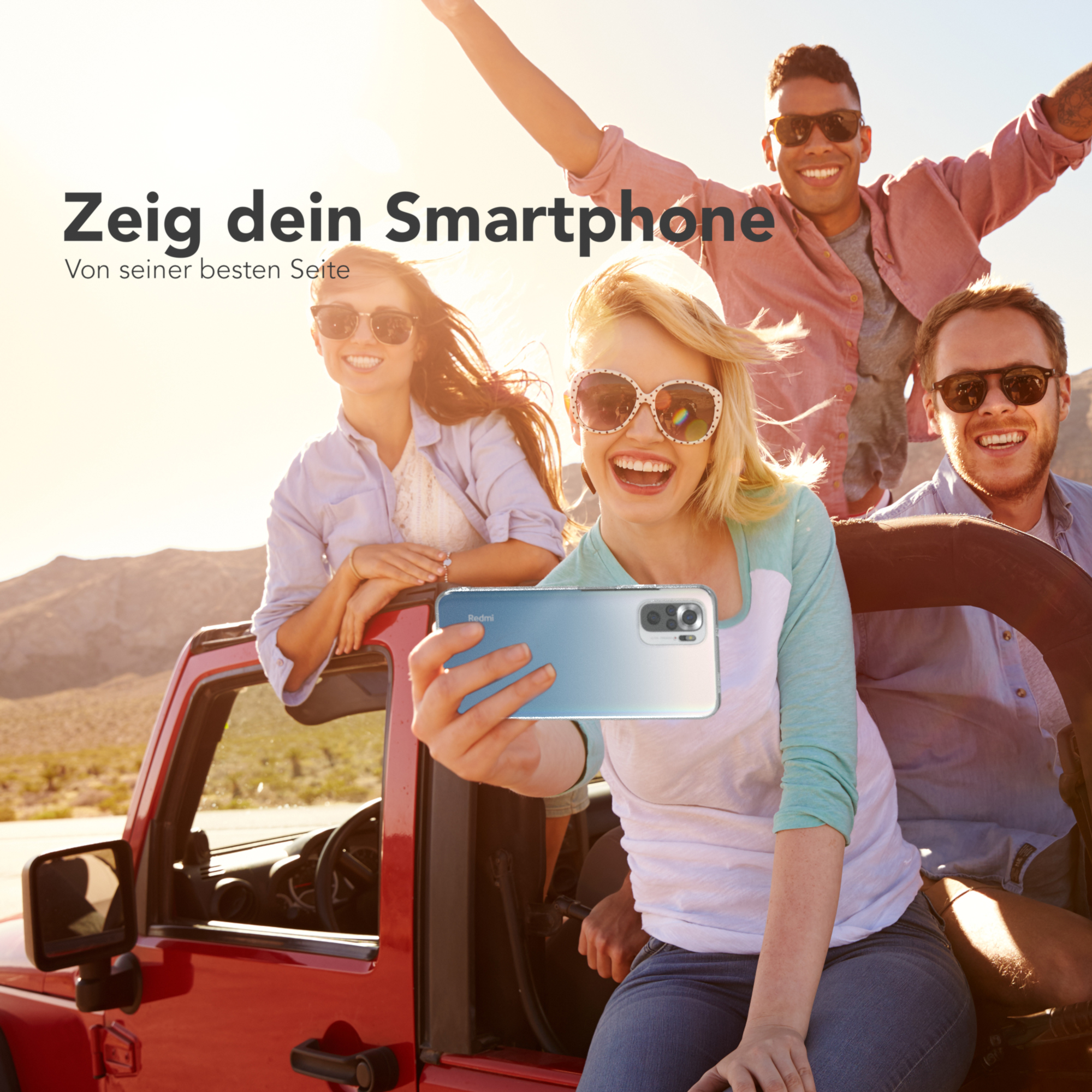 Vier Personen in einem roten Jeep machen ein Selfie mit einem Telefon. Sie lächeln und sind glücklich.