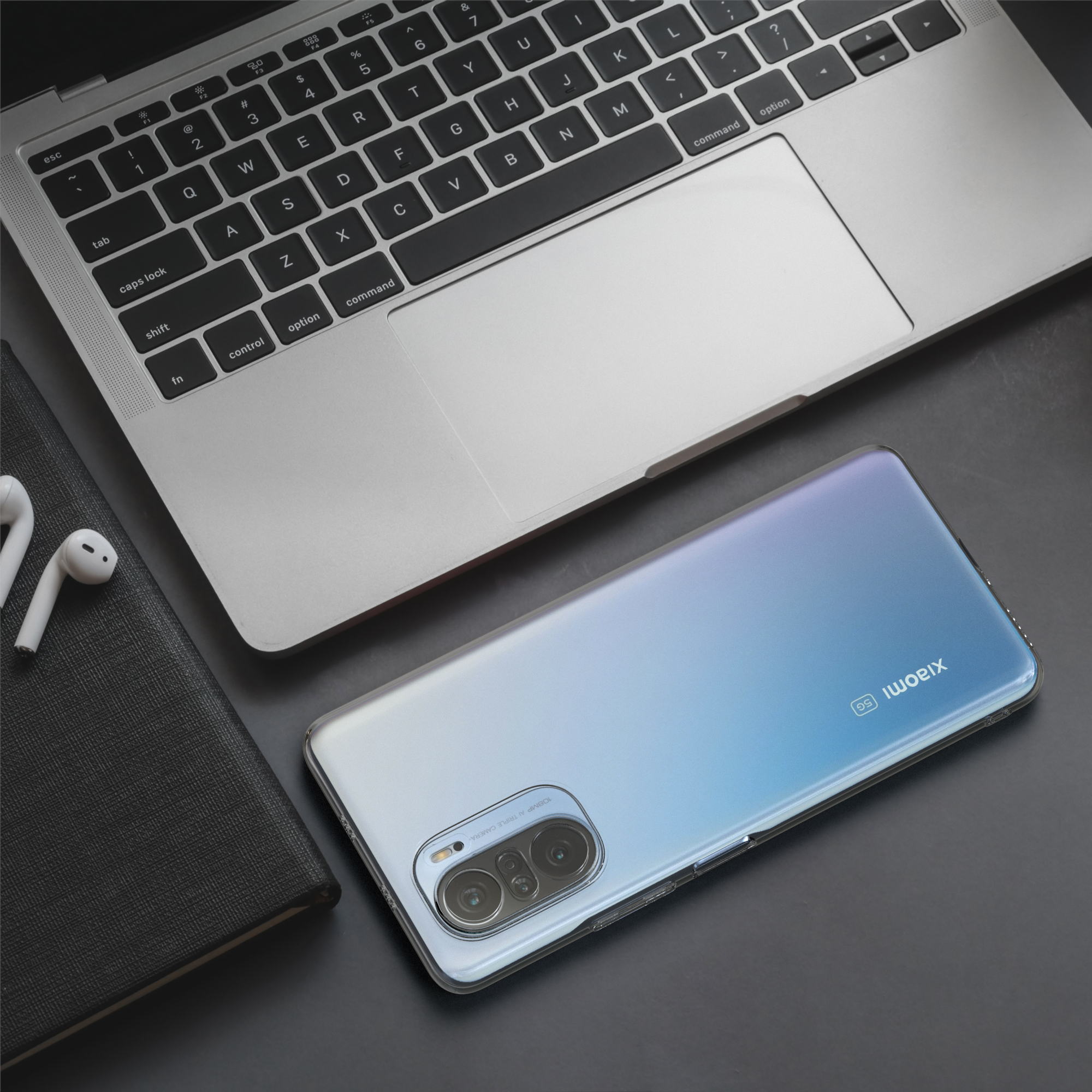 Laptop und Telefon mit transparenter Hülle auf dunkler Oberfläche. Weiße Ohrhörer liegen neben dem Laptop.