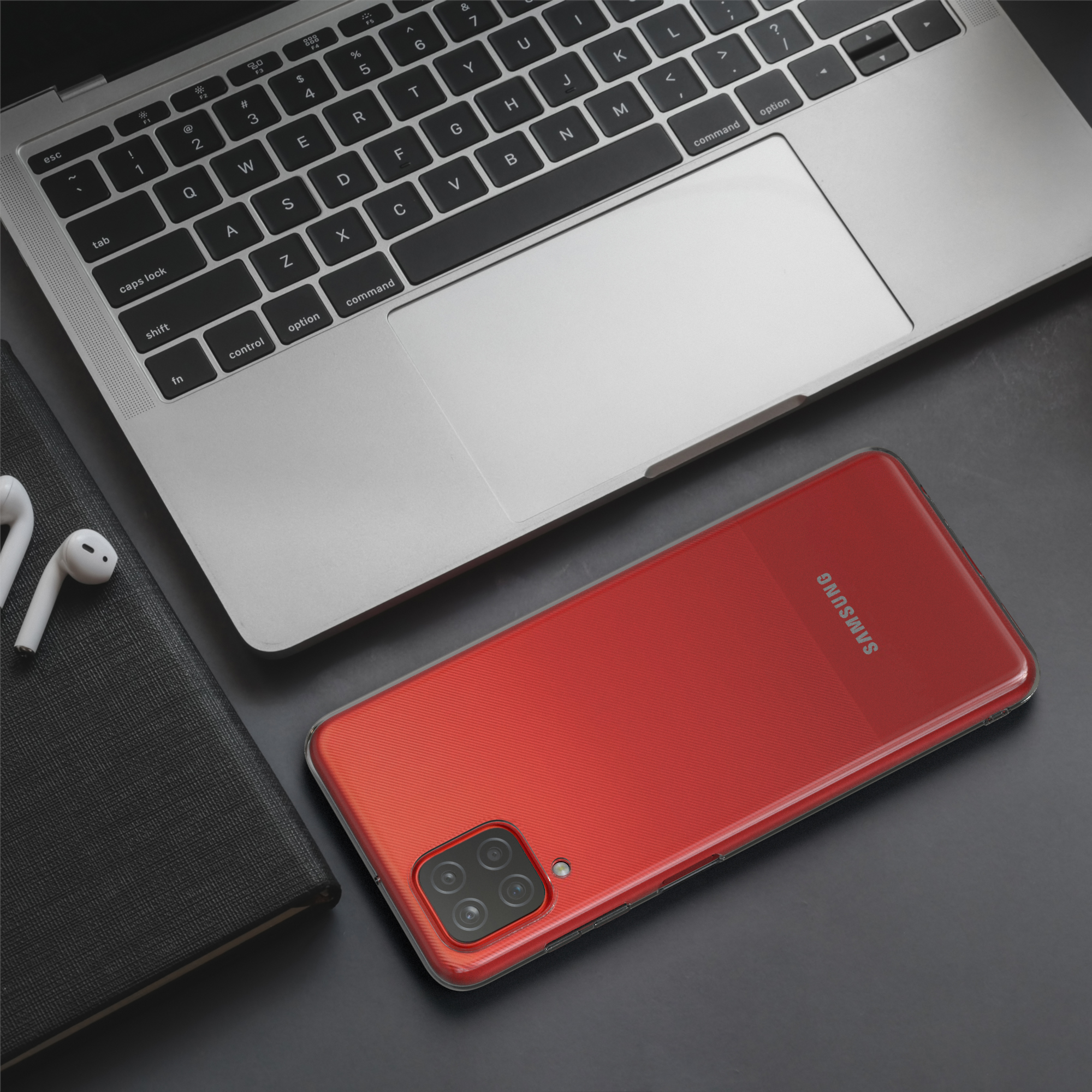 Ein rotes Telefon in einer transparenten Hülle, auf einem Schreibtisch mit Laptop, Notizbuch und Kopfhörern.