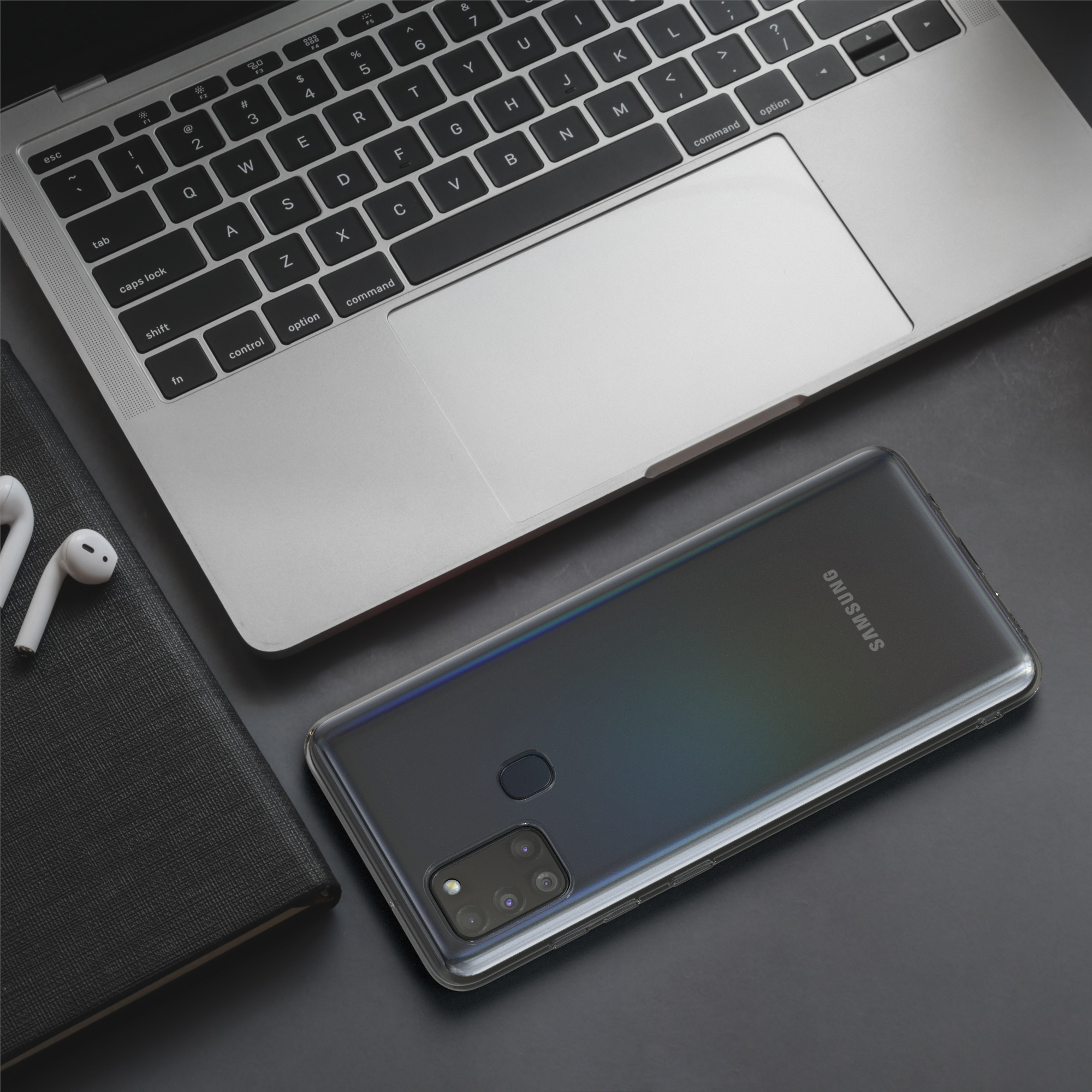 Laptop, Telefon, Ohrhörer und Notizbuch auf dem Schreibtisch. Telefon mit transparenter Hülle.