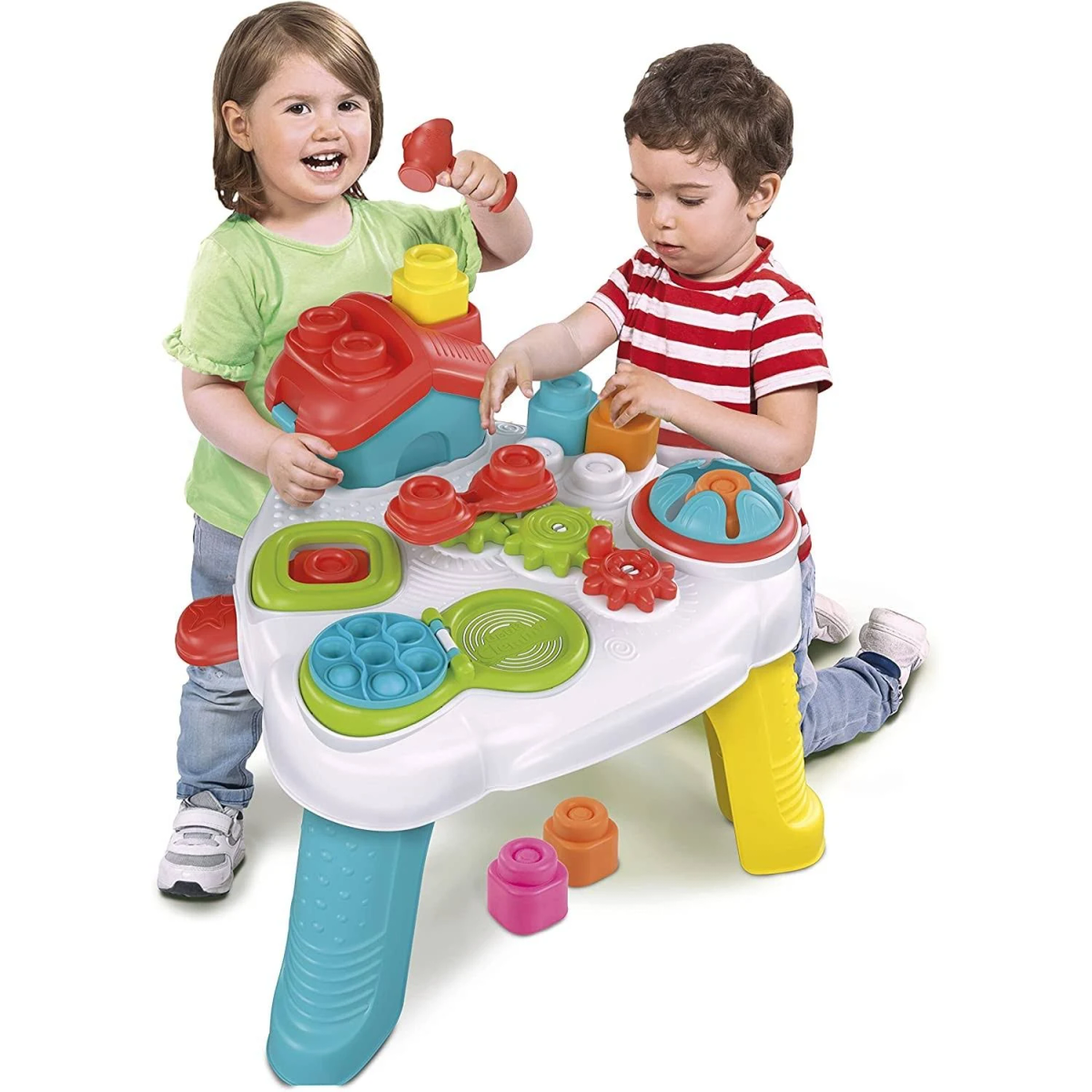 Dos niños juegan con una mesa de juguete, uno con un martillo. Bloques y engranajes de colores en la mesa.