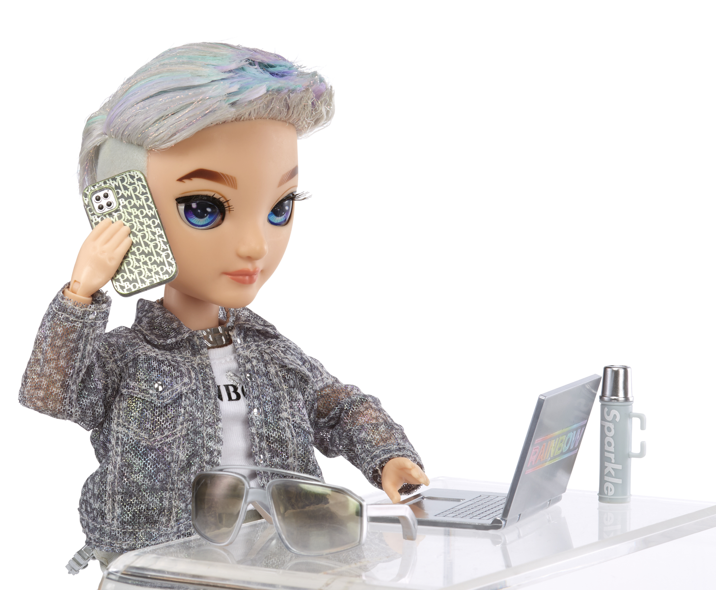 Lalka w kurtce rozmawia przez telefon, używając laptopa i kubka.