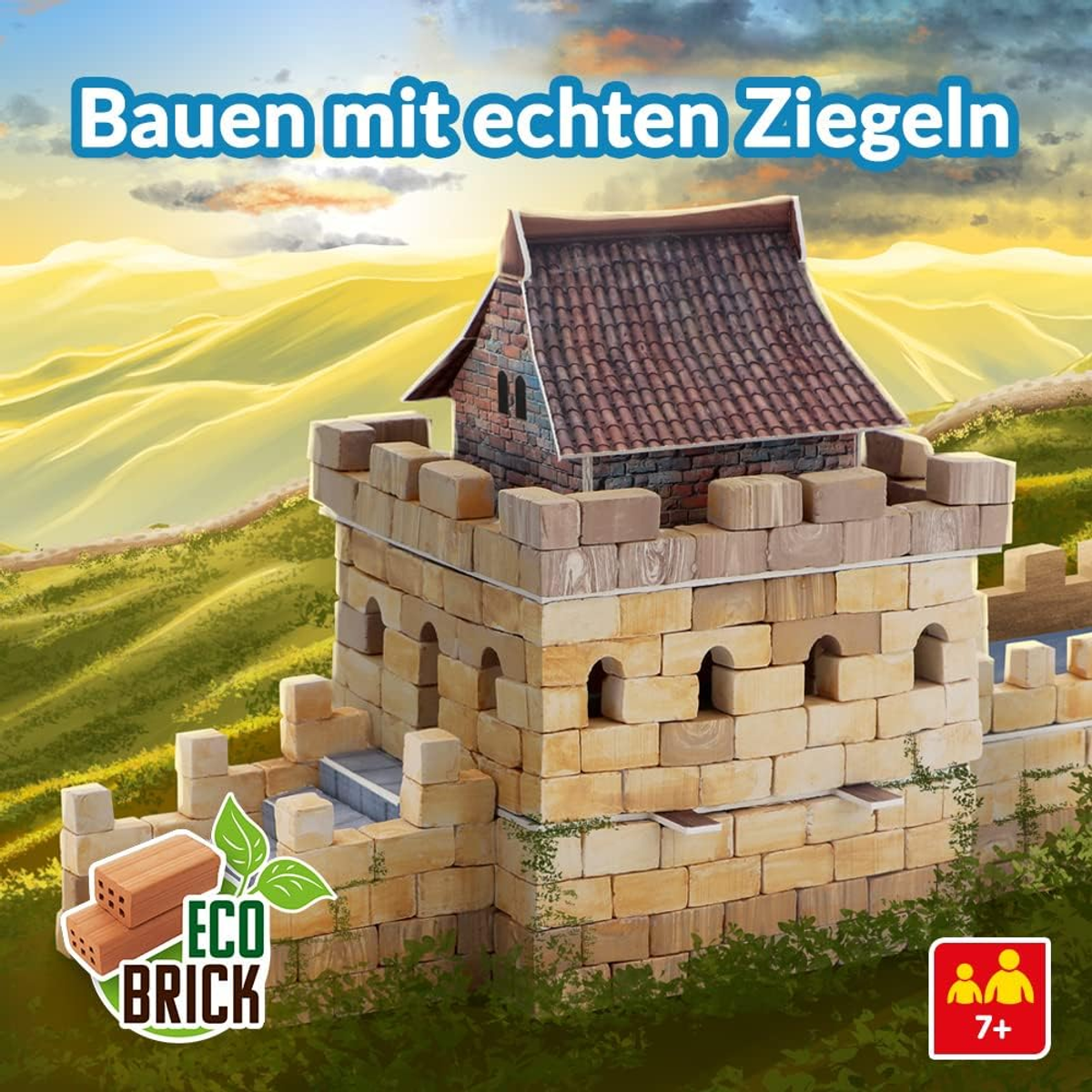 Ein Spielzeugschloss aus Spielzeugziegeln, vor einem grünen Hügel unter blauem Himmel.