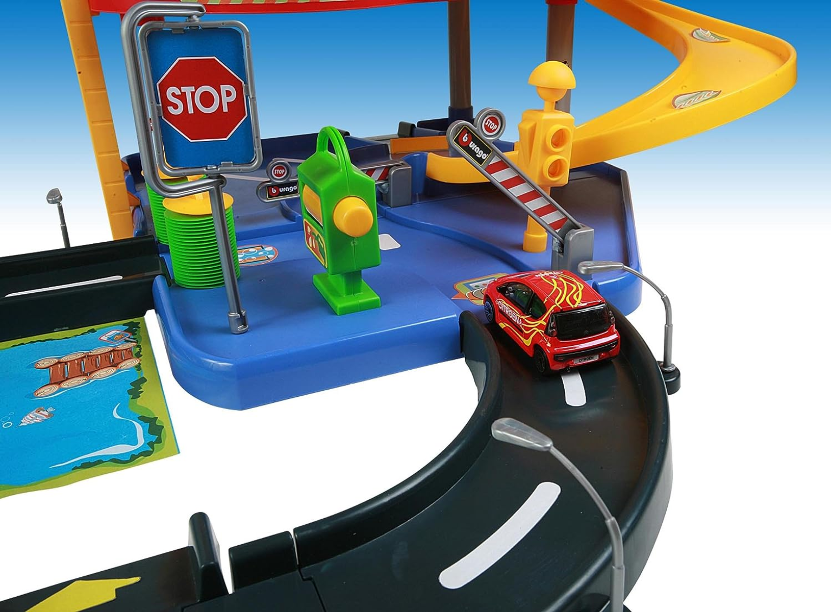 Un juego de garaje de juguete con un coche rojo entrando en una curva. Se ven una señal de stop, una gasolinera y un semáforo.