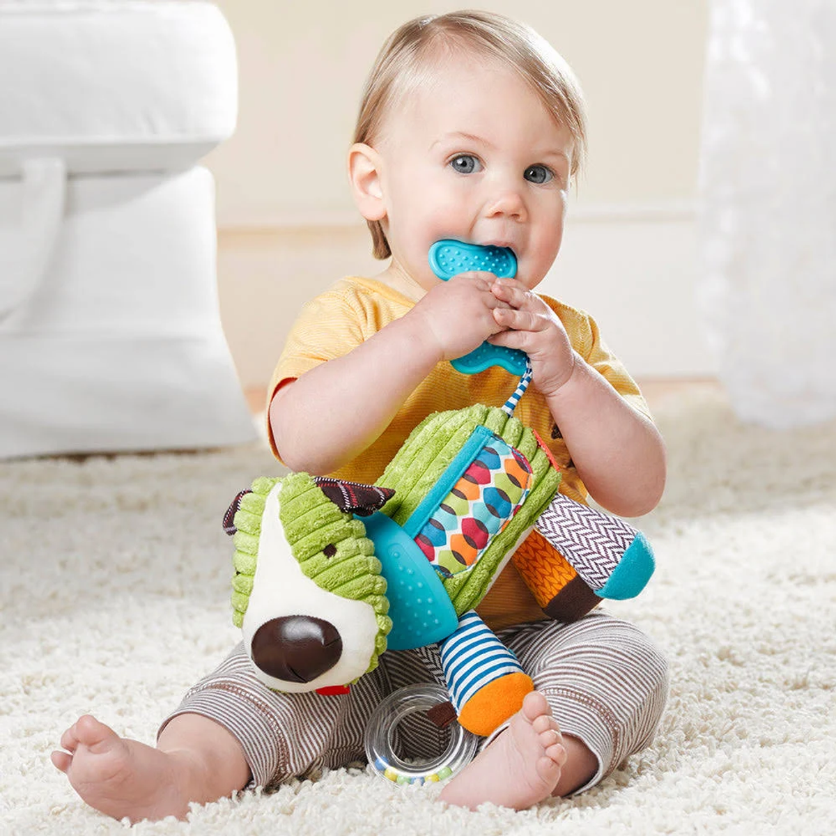 Ein Baby hält einen Spielzeughund und sitzt auf einem Teppich.