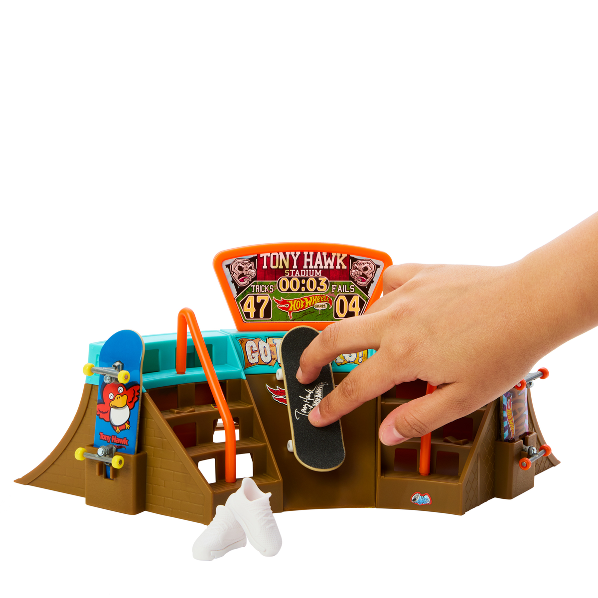 Ręka dziecka z zabawką fingerboard na skateparku z rampami i wyświetlaczami wyników.