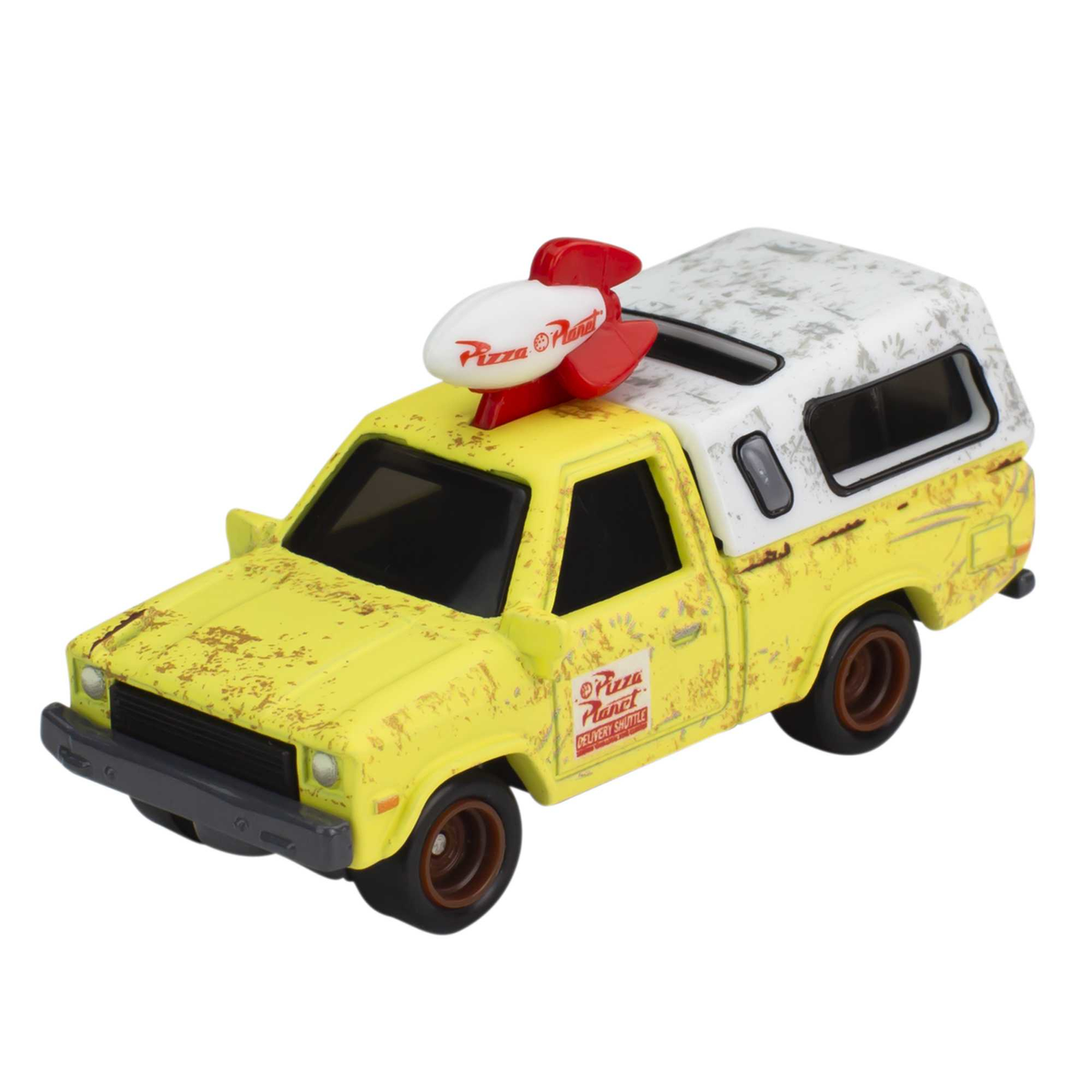 Żółta zabawka Pizza Planet z rakietą na dachu, jadąca po białej powierzchni.