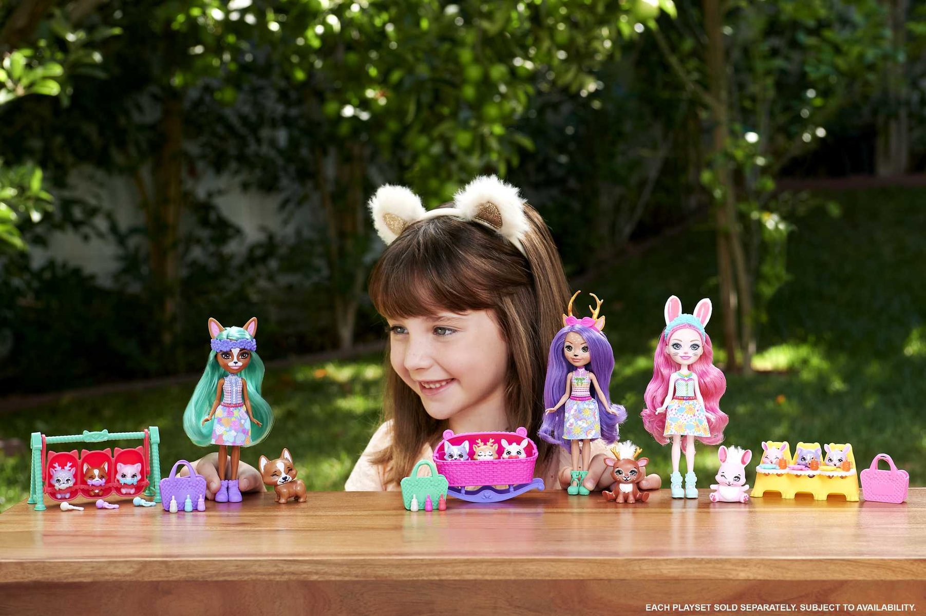 Dziewczynka uśmiecha się do stołu z lalkami i akcesoriami. Lalki mają uszy zwierząt.