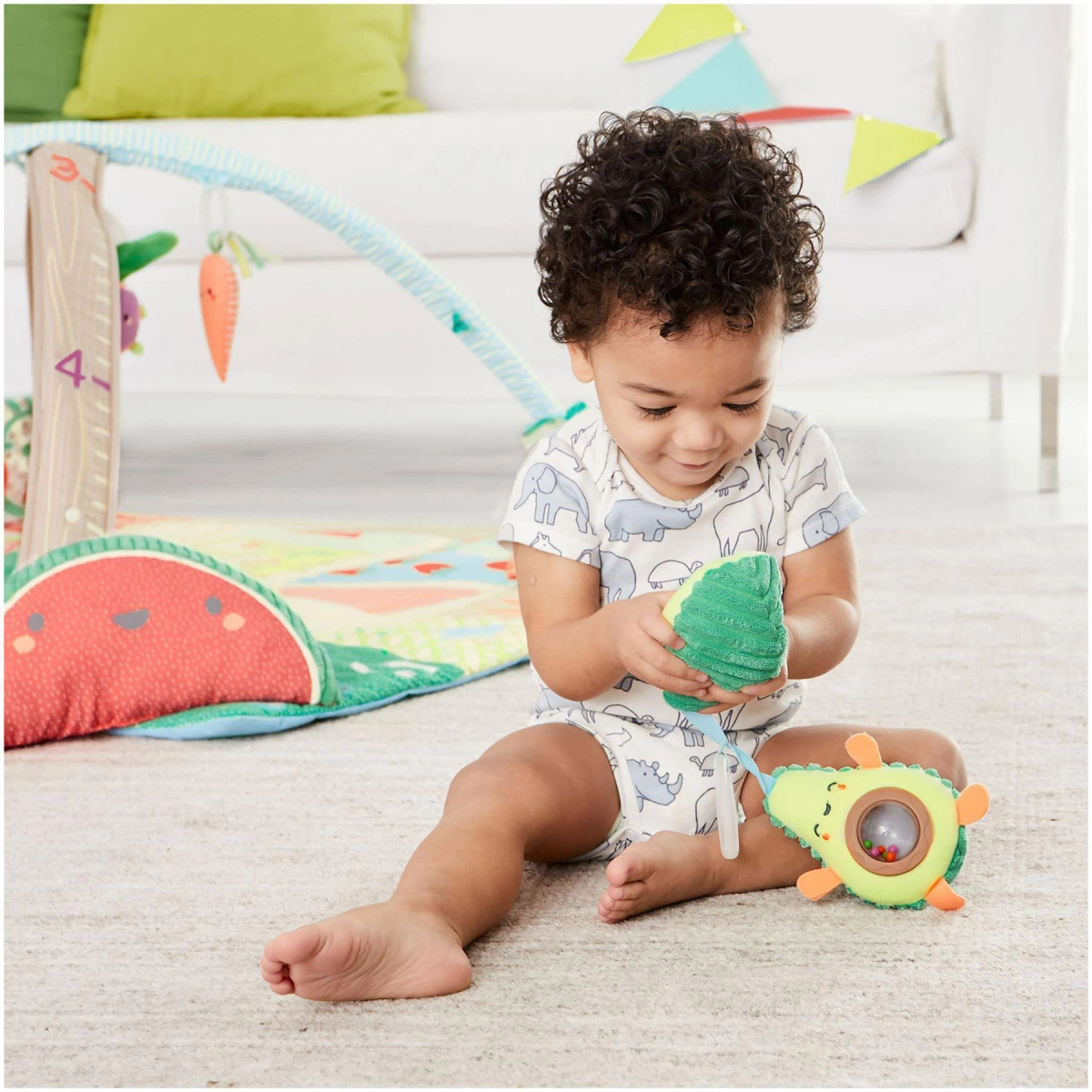 Ein Baby sitzt auf einem Teppich und spielt mit einem grünen Avocado-Spielzeug mit einem Auge.