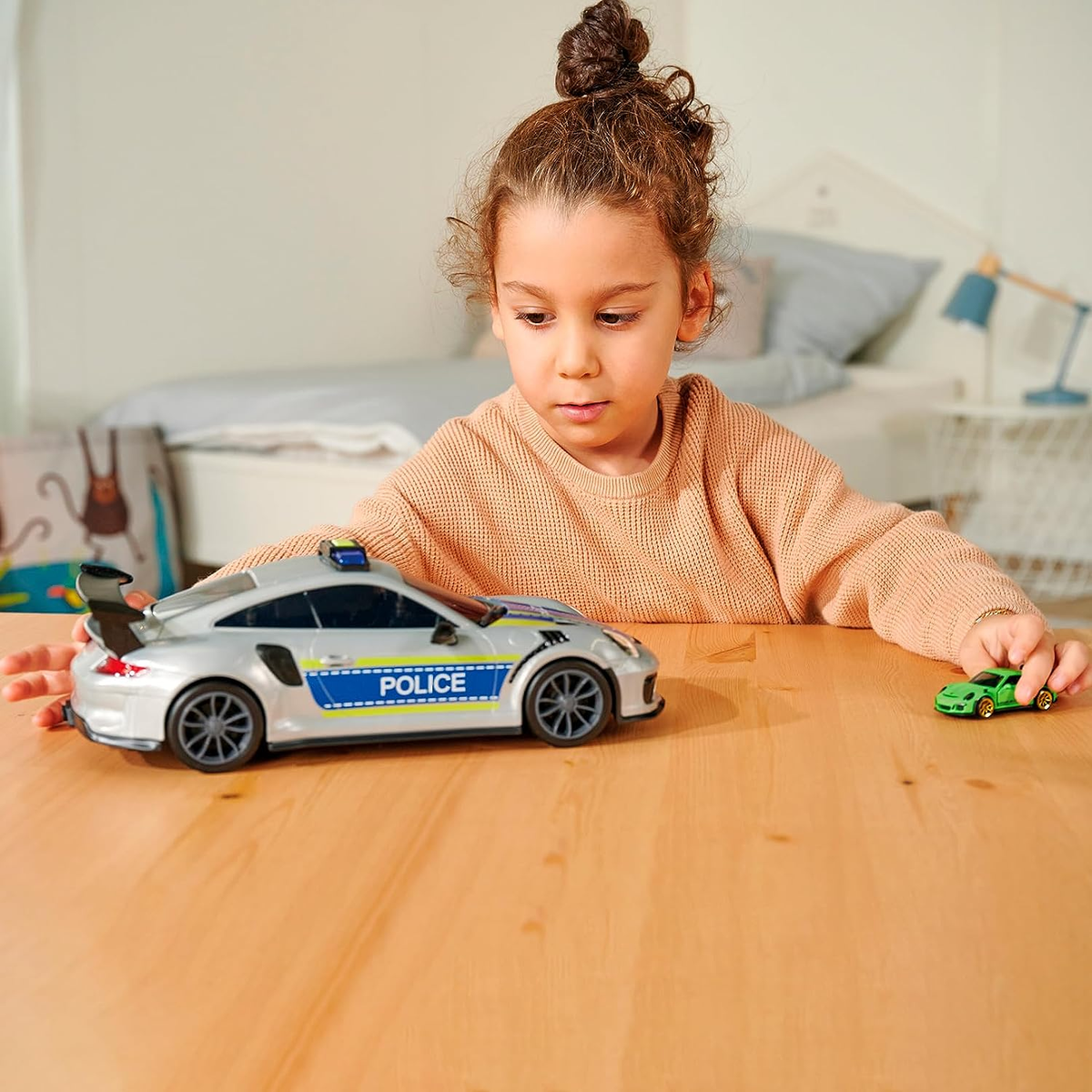 Un niño juega con coches de juguete. Un coche de policía plateado y un coche verde sobre una mesa de madera.