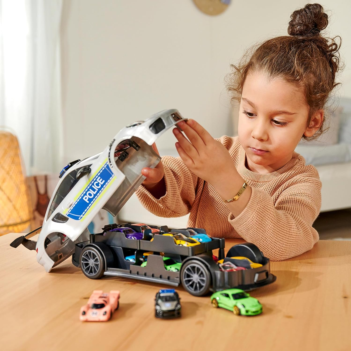 Una niña juega con un camión de juguete lleno de coches de juguete. Coches rosas y verdes.