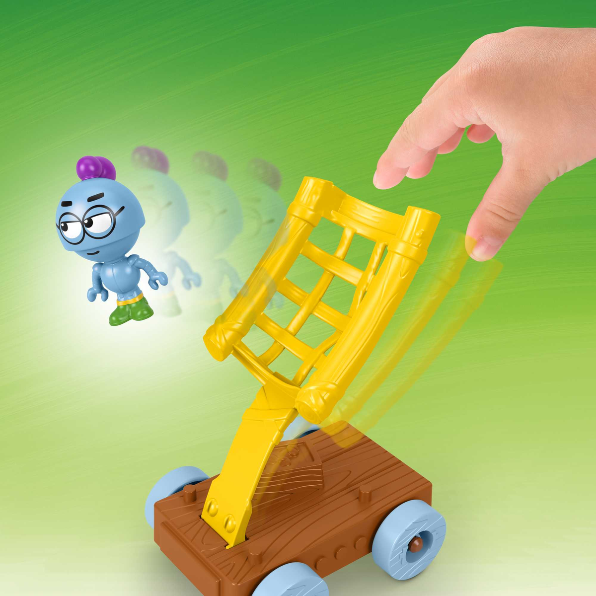 Una mano opera una catapulta de juguete amarilla. Una figura azul está en el aire.