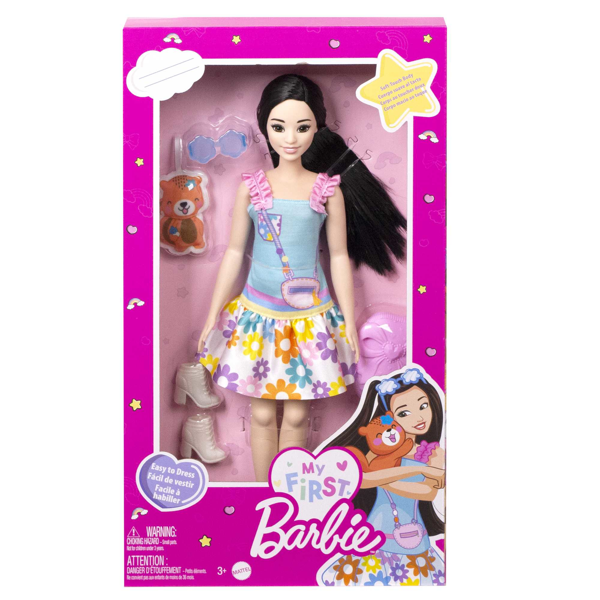Eine Barbie-Puppe in einer Box mit Zubehör. Sie hat schwarze Haare, ein blaues Kleid und einen Bären.
