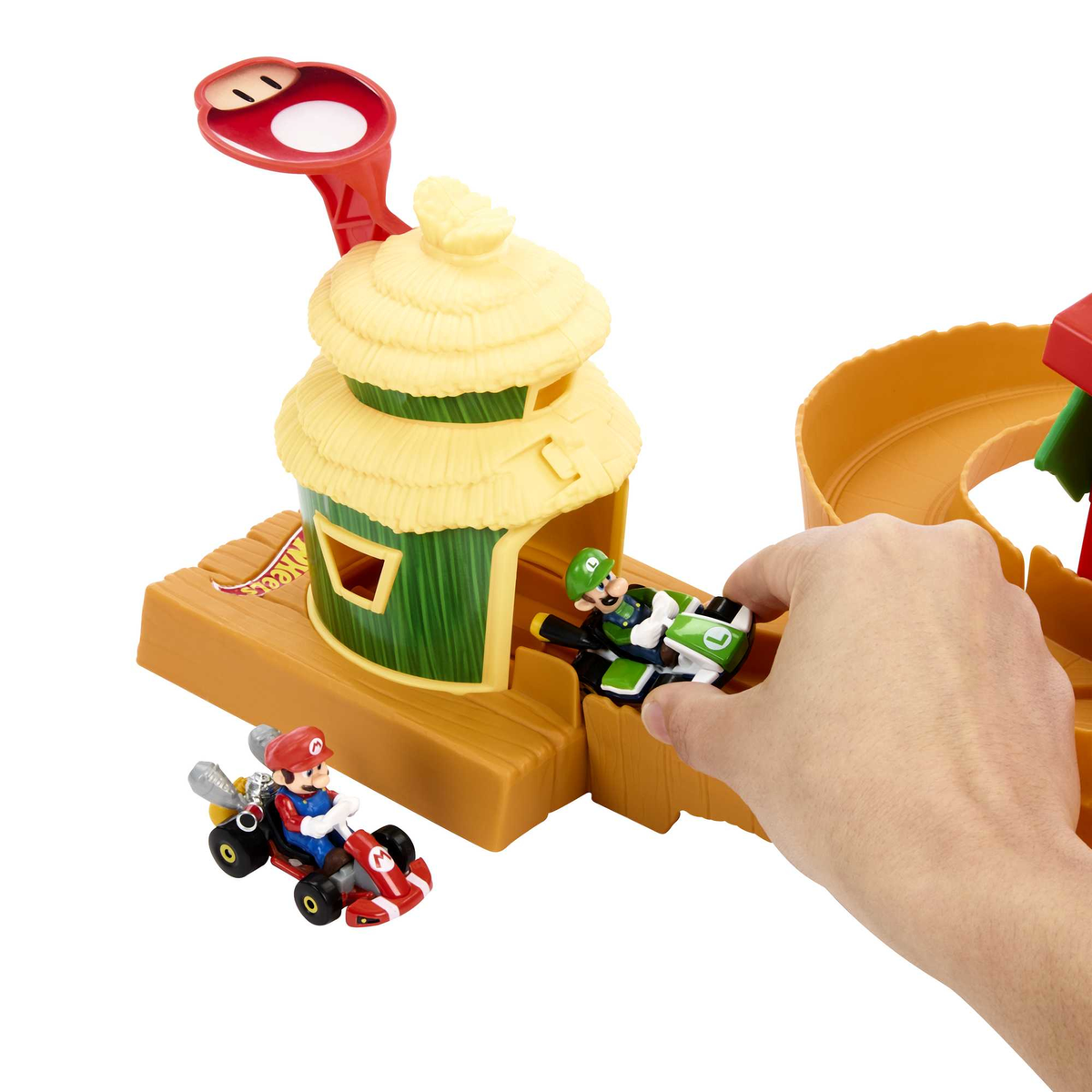 Pista giocattolo di Mario Kart con personaggi e una mano che raggiunge un'auto.