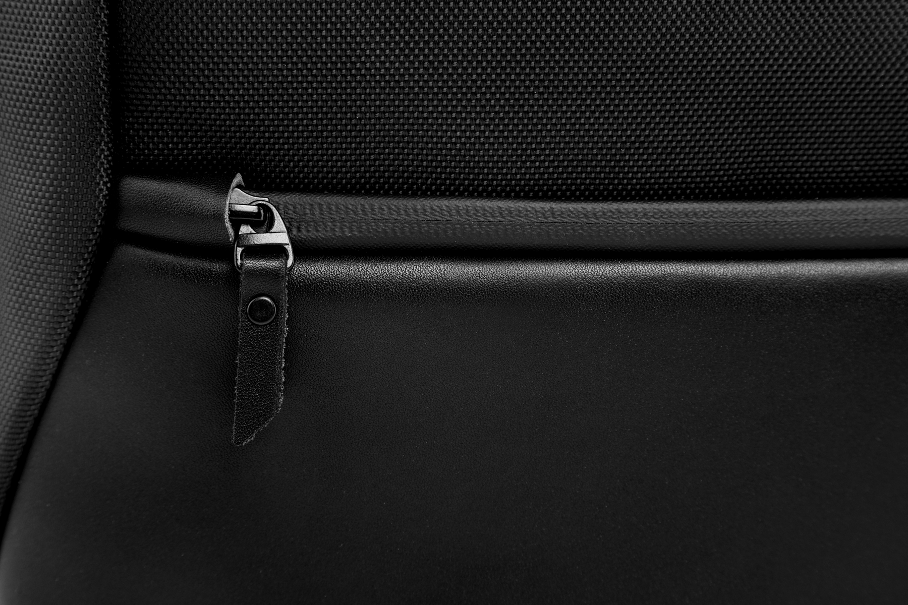 Primo piano di una borsa in pelle nera con cerniera e cinturino. Lo sfondo è nero.