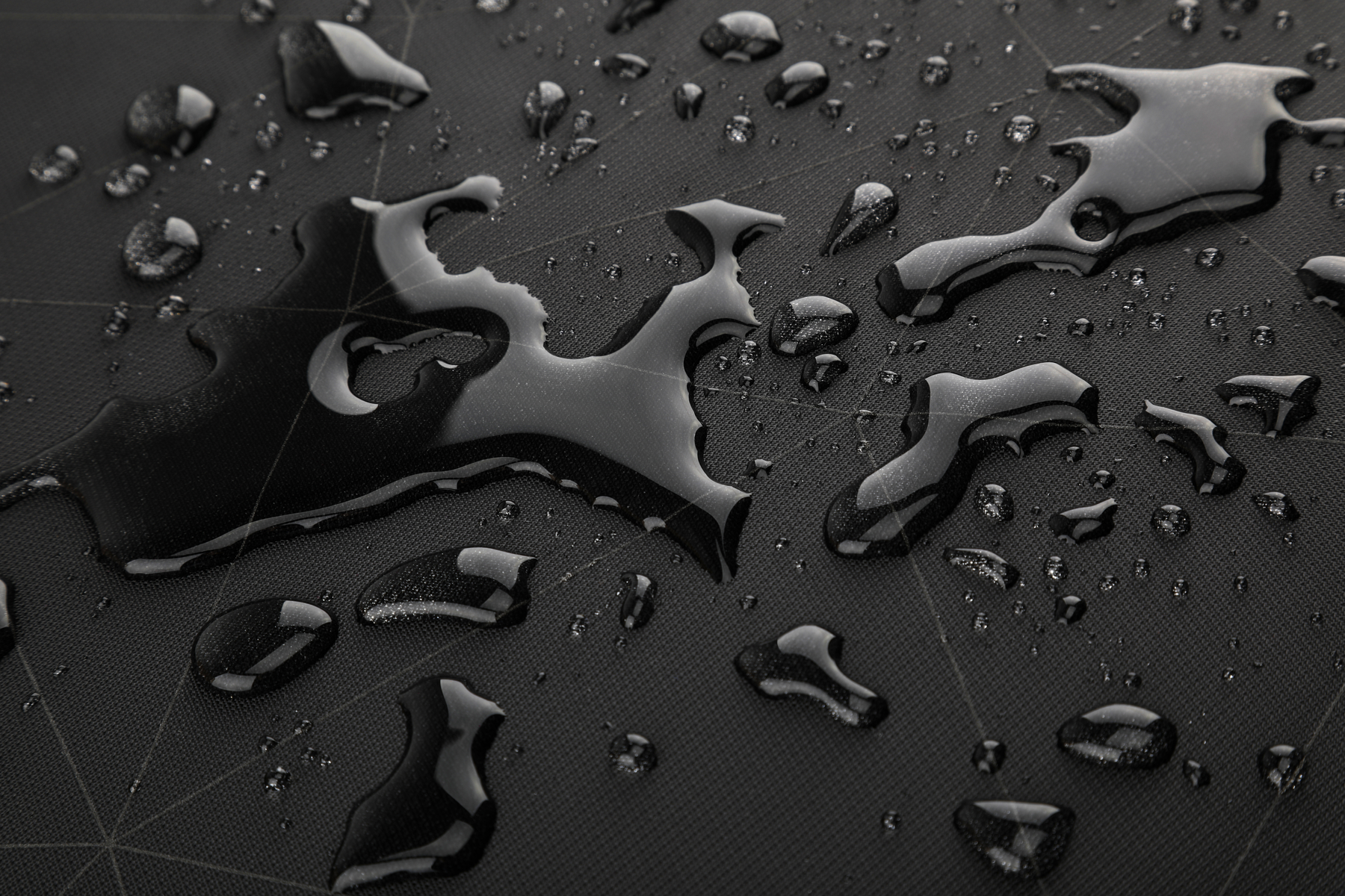 Gocce d'acqua su una superficie nera e strutturata, creando forme irregolari.