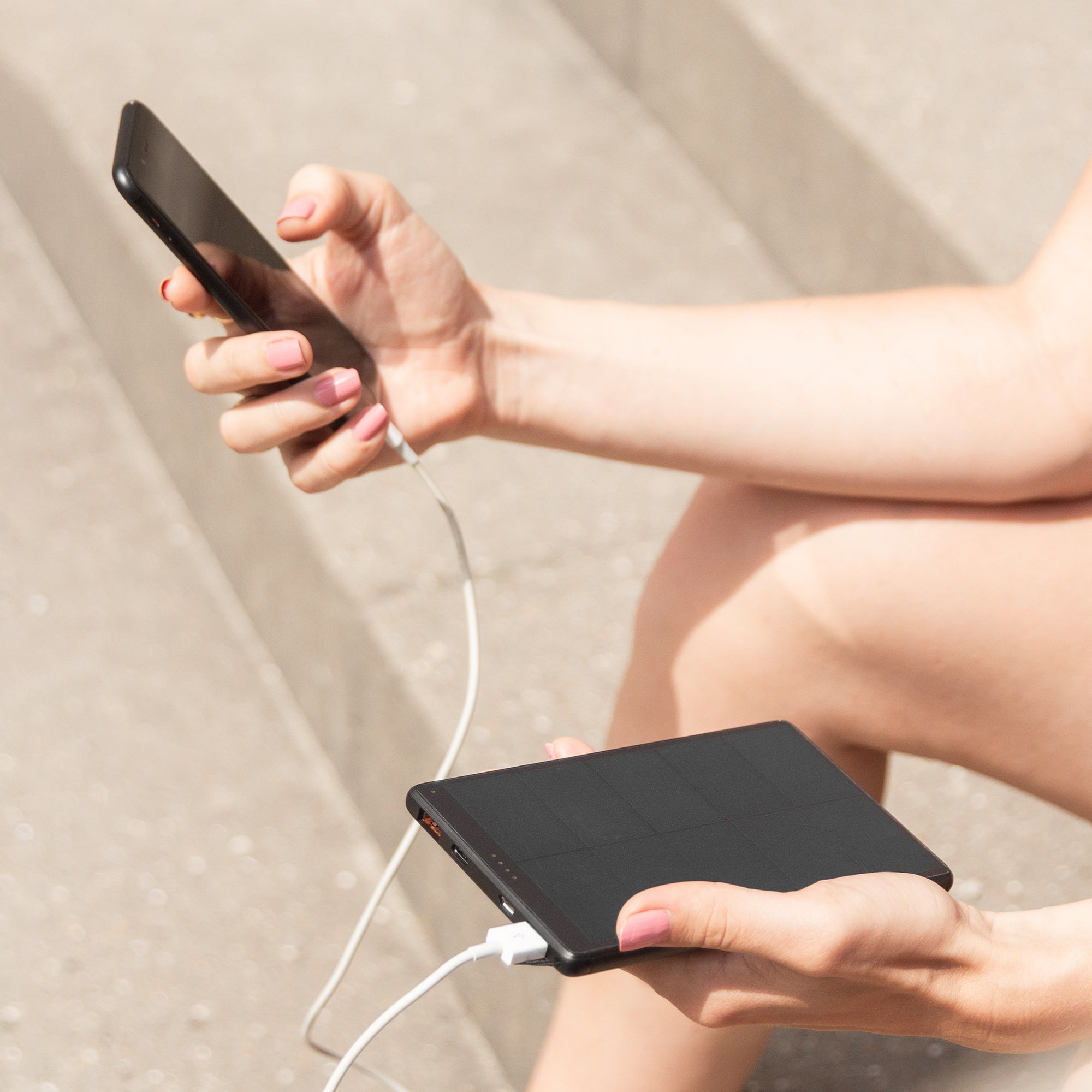 Die Hände einer Person halten ein schwarzes Telefon und eine schwarze Powerbank mit einem weißen Ladekabel.