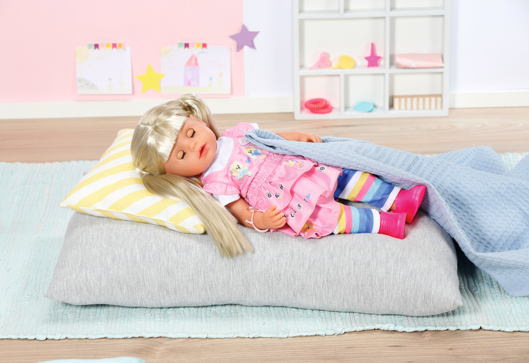 Babypuppe schläft auf einem Kissen, mit einer Decke bedeckt. Rosa Pyjama, blondes Haar.
