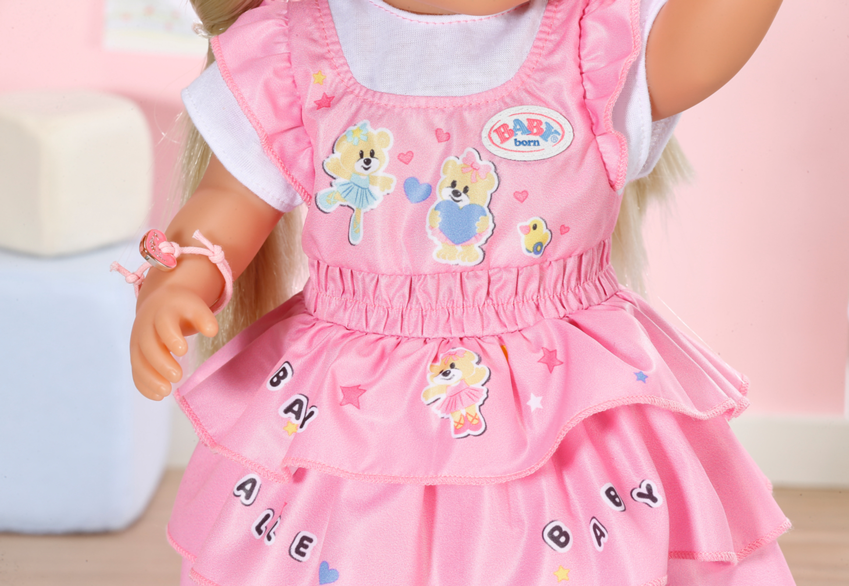 Puppe in rosa Kleid mit Bär-Design, vor rosa Hintergrund.